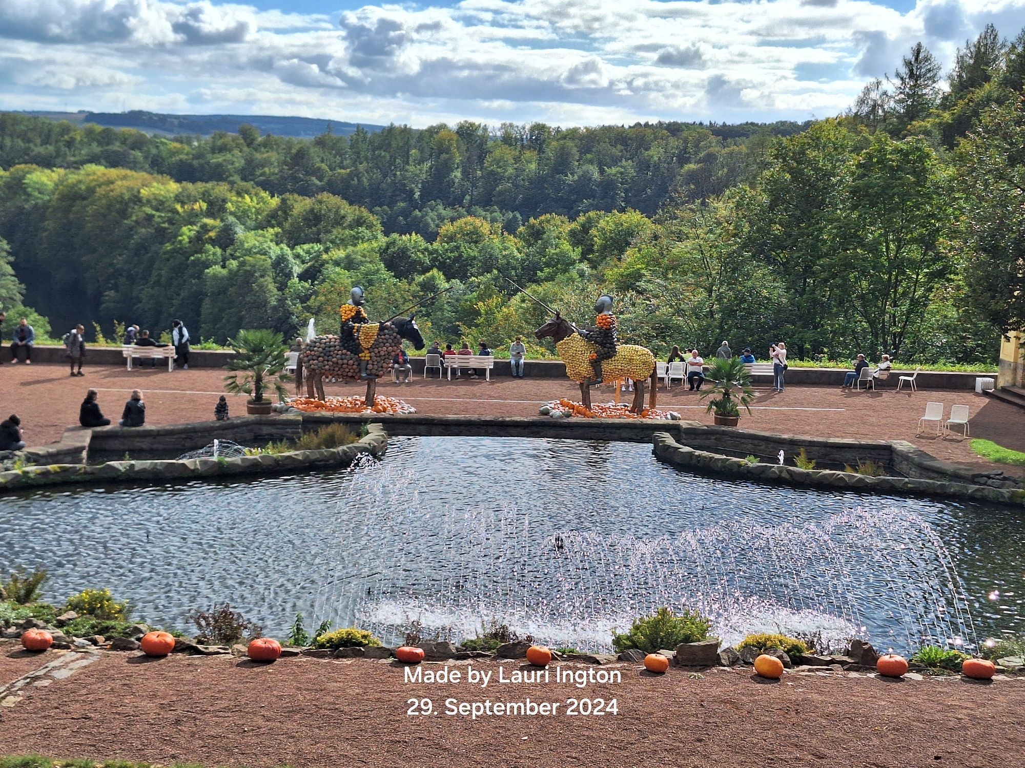 Blick auf einen angelegten Brunnen mit Fontäne
Im Hintergrund sieht man 2 Ritter auf Pferden welche aussehen, als wenn sie aus vers Kürbissen beständen