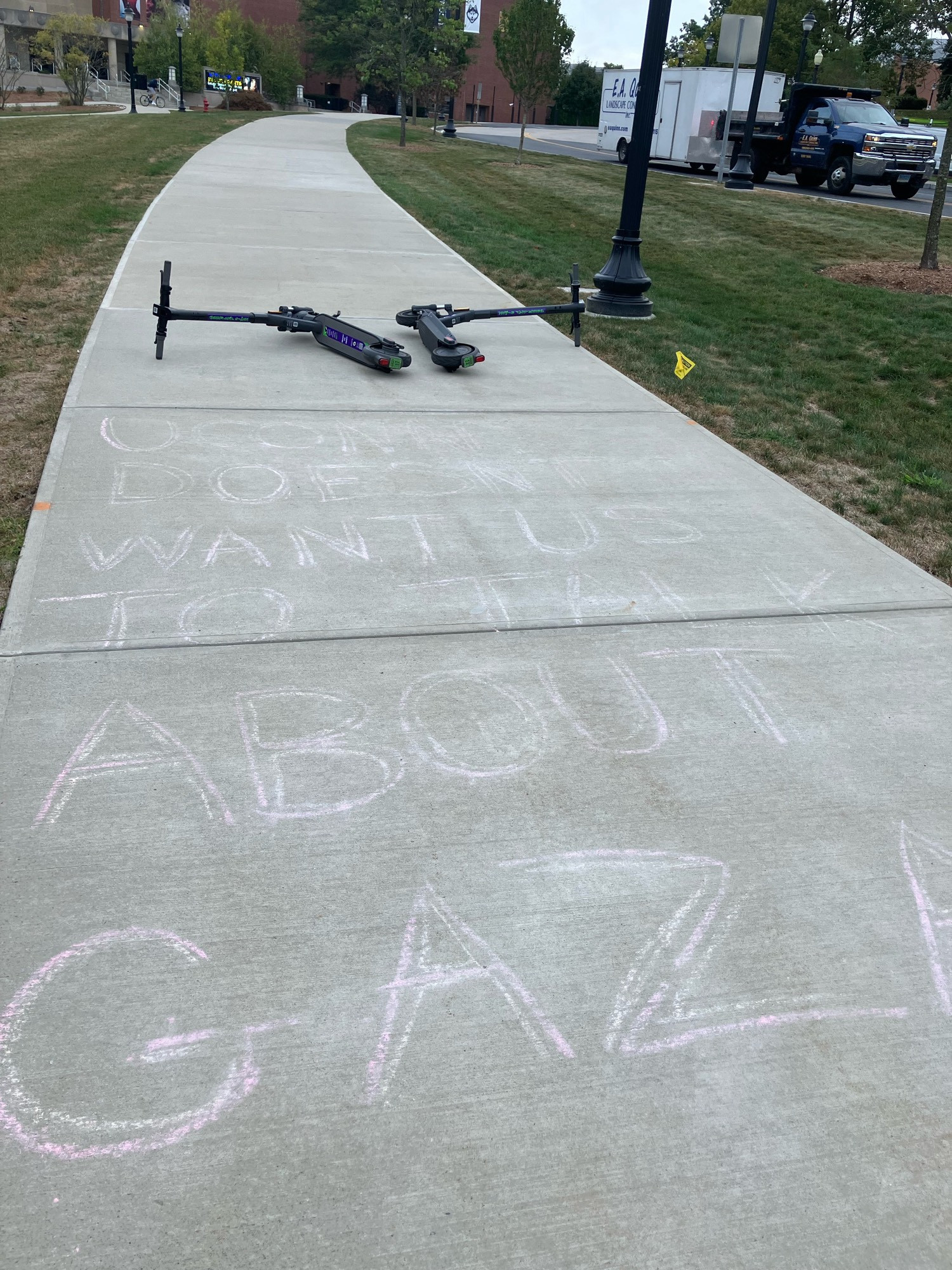 Two scooters, both on their sides, blocking walkway with “UConn doesn’t want us to talk about Gaza” written in chalk.