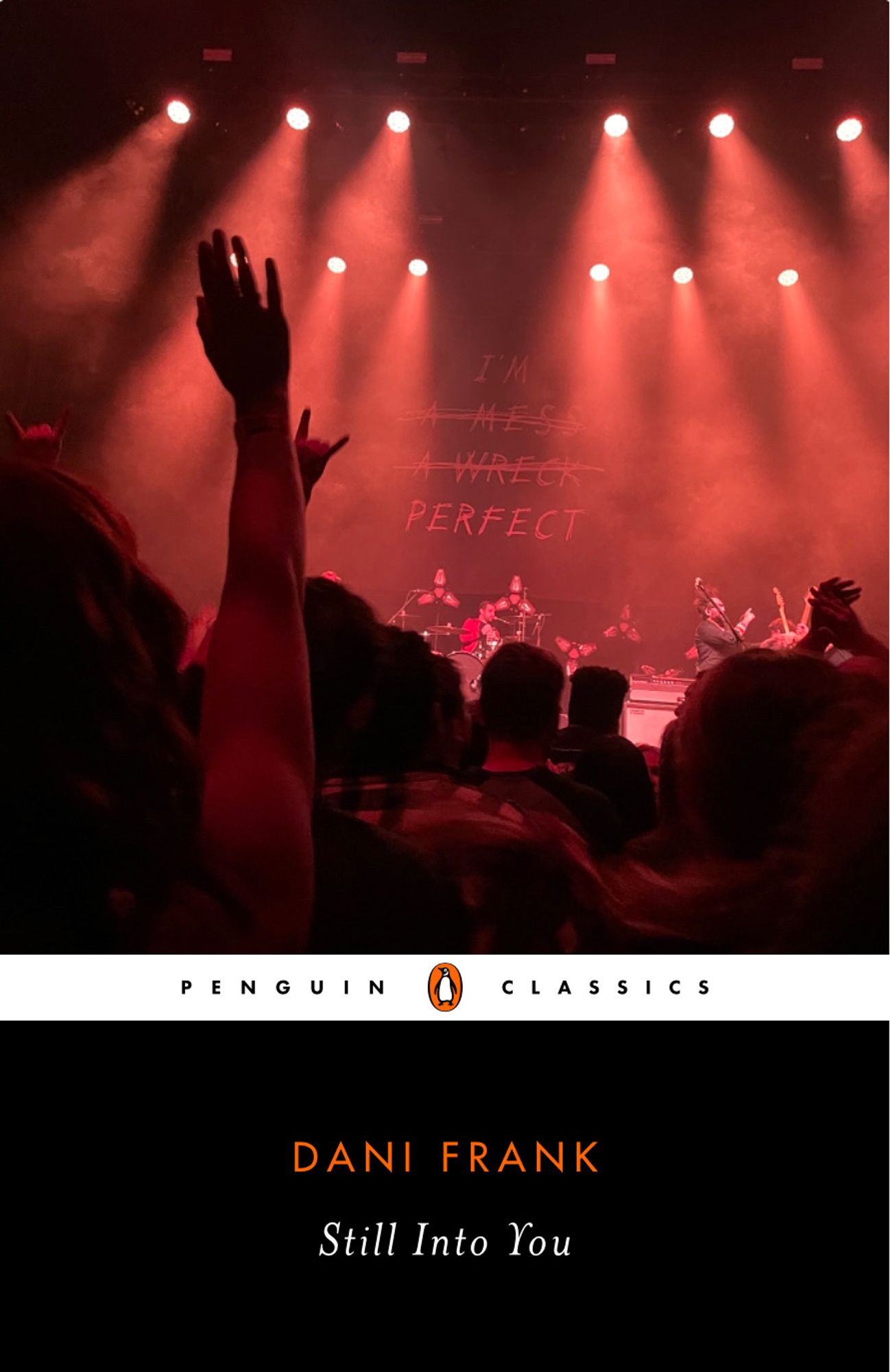 Mock-up of a Penguin Classics book cover with the title Still Into You by Dani Frank in a black panel at the bottom of the cover. The top portion has an image of a crowd facing a stage seen from a member of the audience. Several people have arms raised to the band on stage who can barely be seen through the people. Above the band in large handwritten looking text are the words “I am”. Underneath is scratched out “a mess” and “a wreck”. Below those and not scratched out is written “Perfect”.