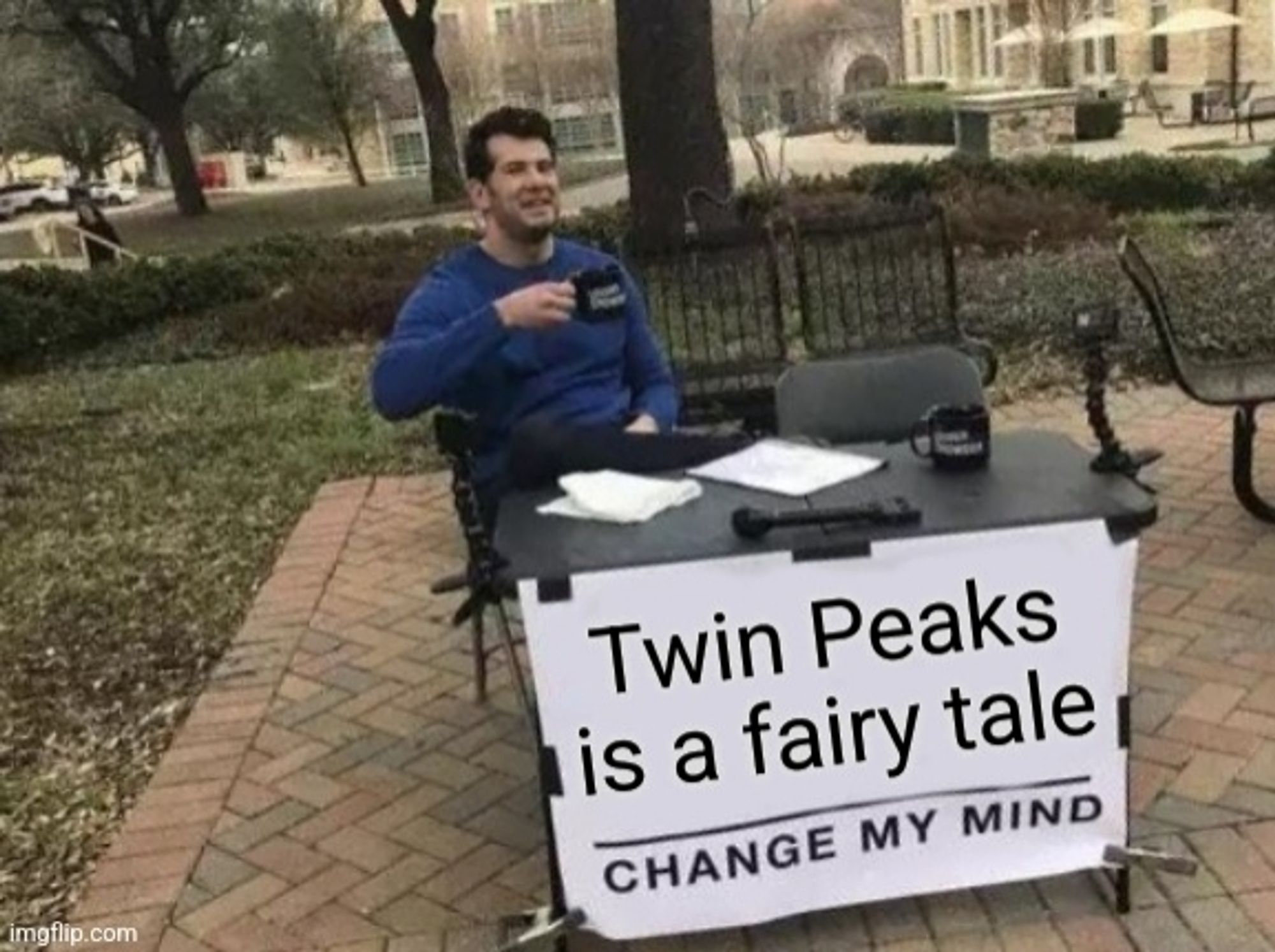 "Change My Mind" meme. Man in park sitting at a table with a sign reading "Twin Peaks is a fairy tale – chage my mind"