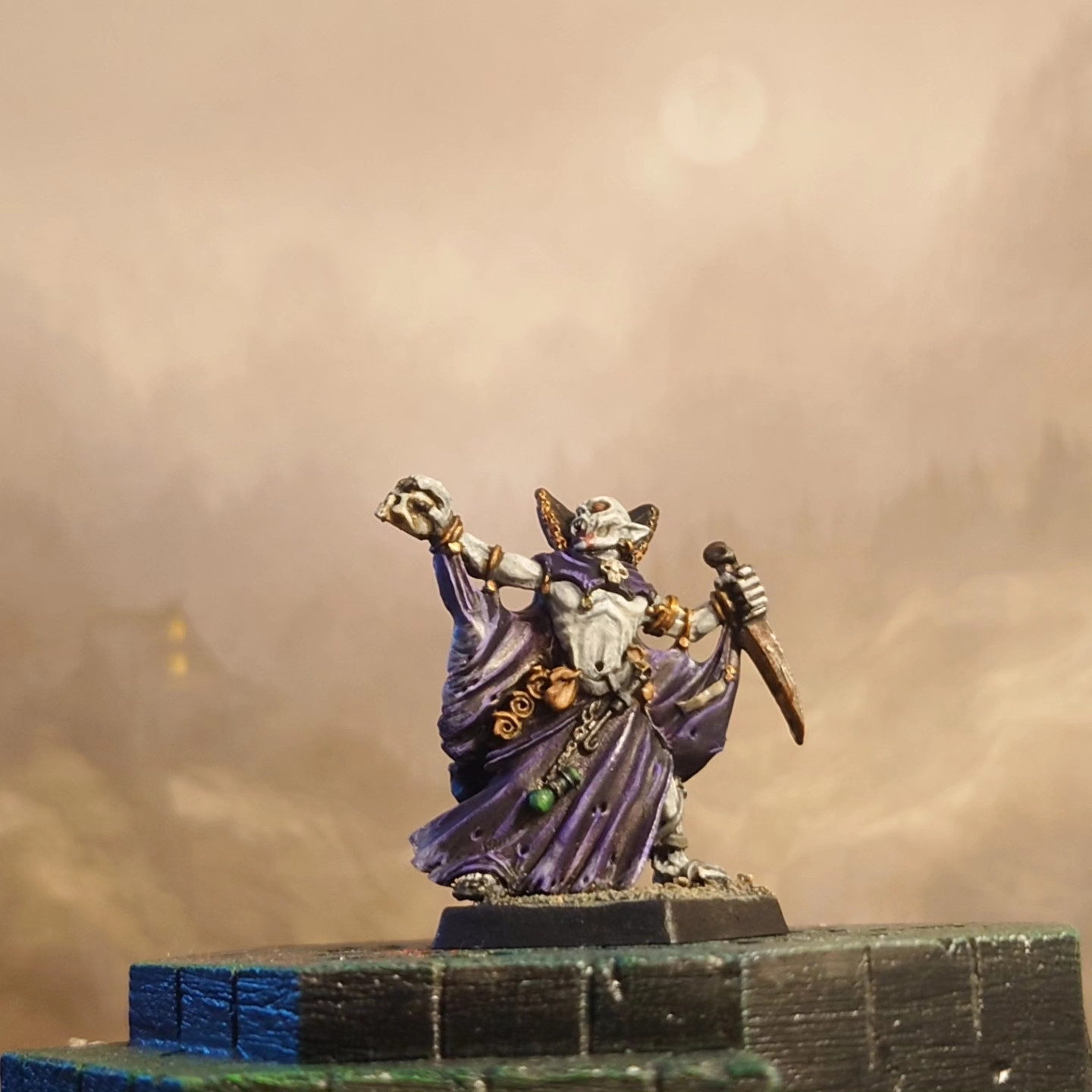 A purple robed vampire raises a skull over an obsidian plinth.