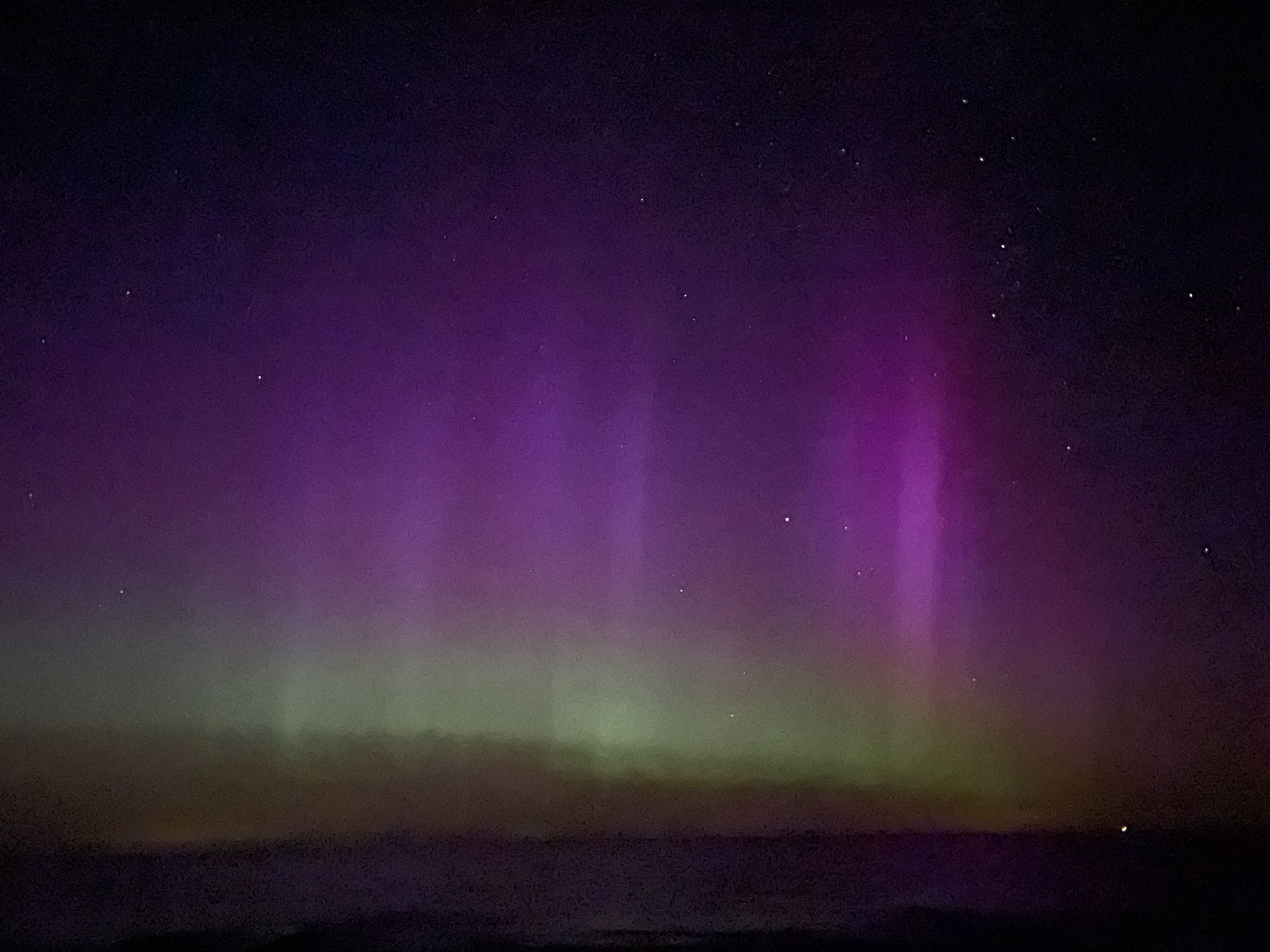 Foto von Polarlicht , es schimmert im oberen Bereich Lilafarbn u im unteren Bereich Gelb- Grünlich.