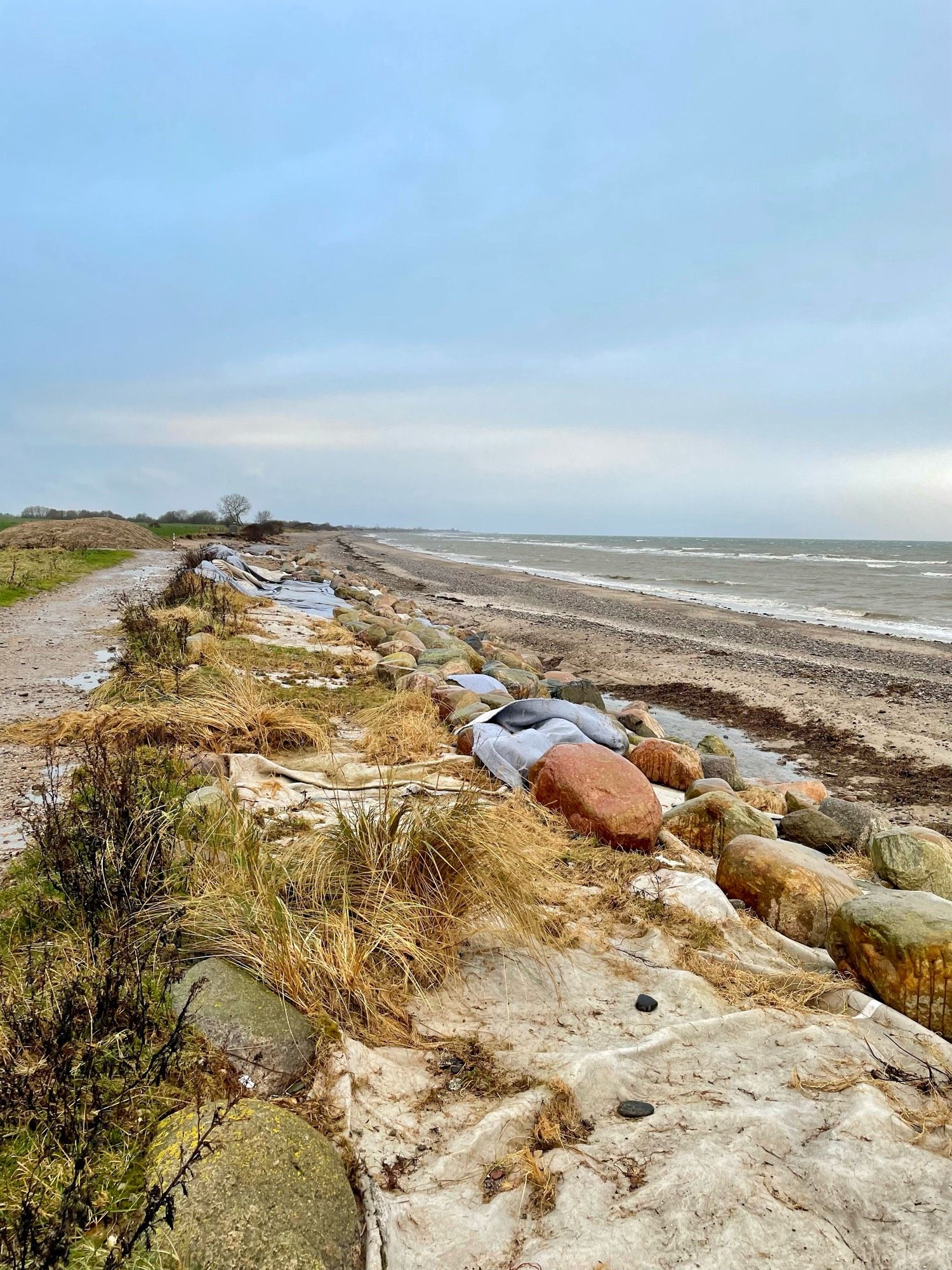 Strand , es ist kalt u windig. Leichter Schneeregen. Himmel hellgrau. Wasser dunkelgrau. Kein feiner Sandstrand. Hier Steinstrand. Wind hat viel Algen u allerlei feine Sachen an Land gespült.