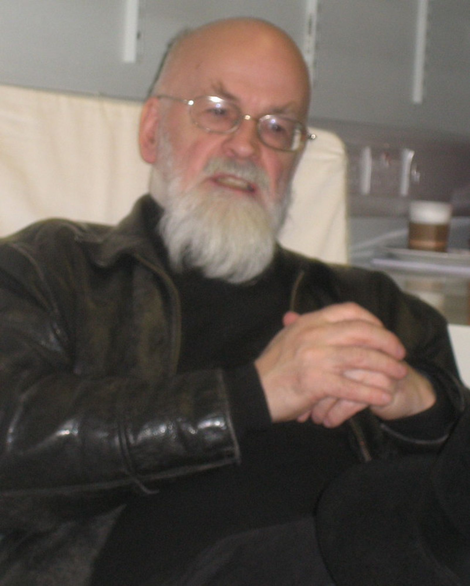 Picture of Terry Pratchett, English author, bald, white-bearded, eyeglasses-wearing white man, about 61 years old then (in 2010), wearing his signature black leather jacket and looking pensive. The photo was stolen from bookwitch.wordpress.com/interviews/terry-pratchett-i-know-the-books-have-their-heart-in-the-right-place/