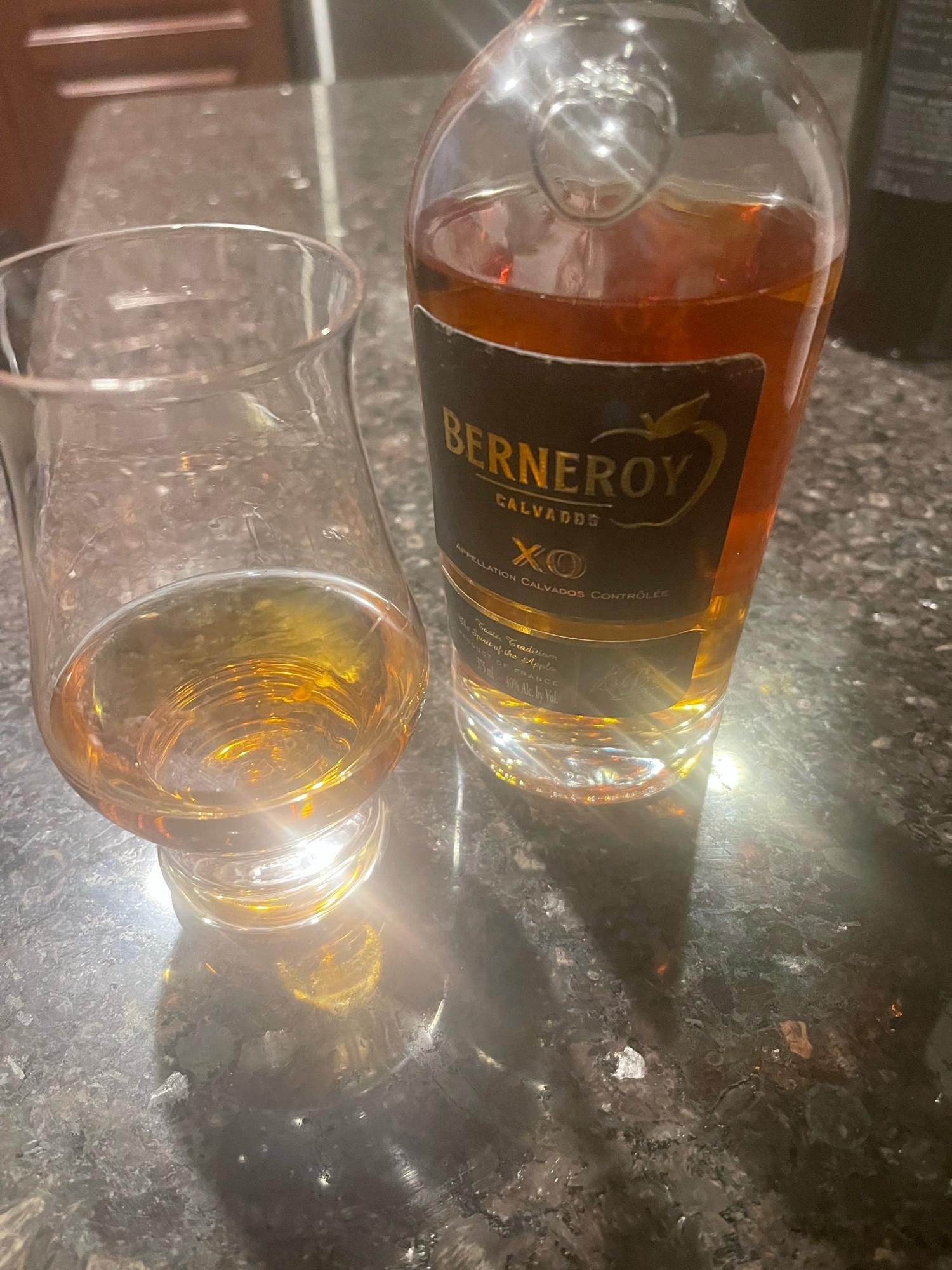 Less-than-full 375 ml bottle of Berneroy XO and a glass containing a neat shot. High lens flare effect (all natural).