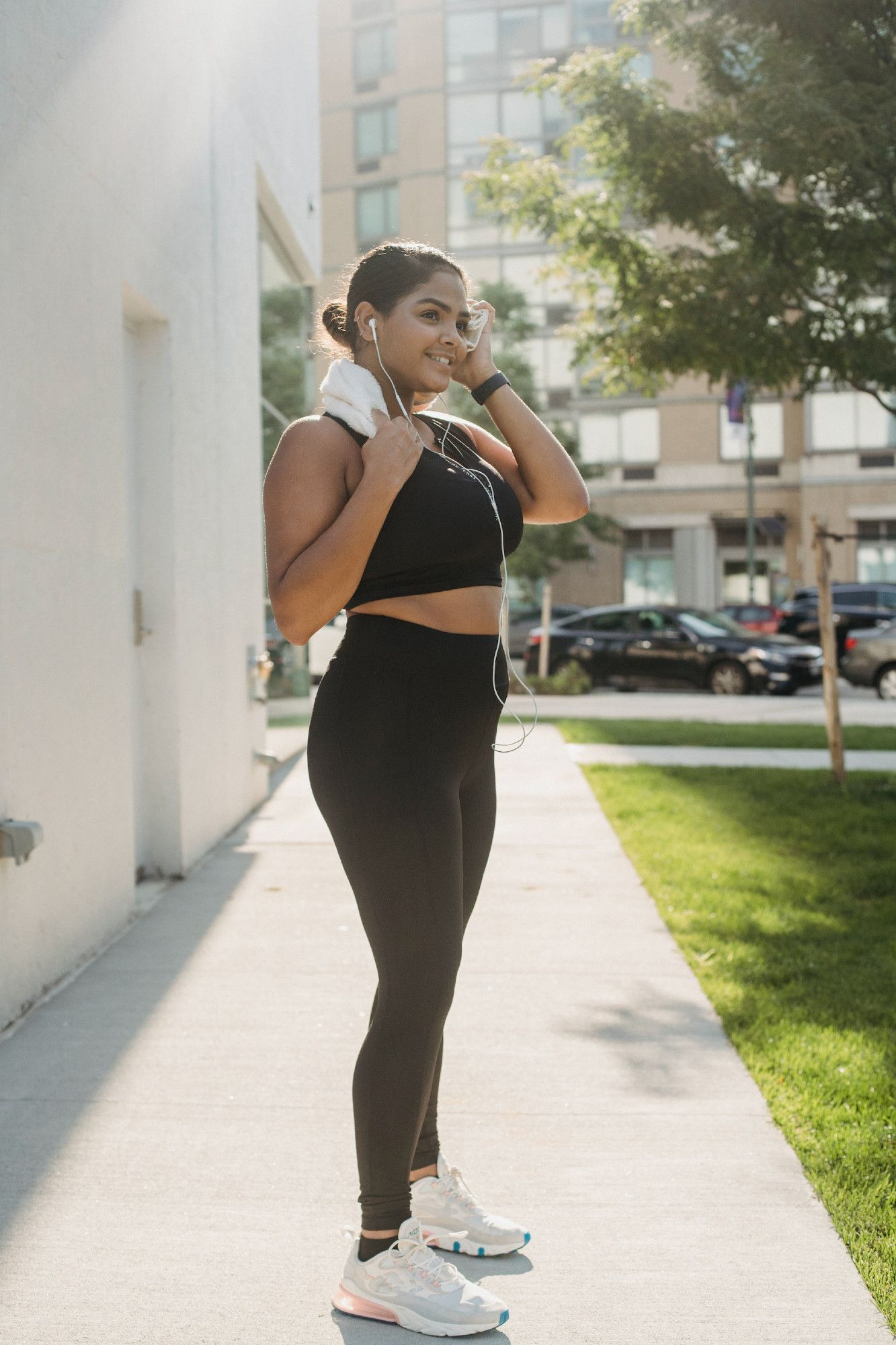 Woman in workout clothes, running shoes, earbuds standing outside on a sunny day