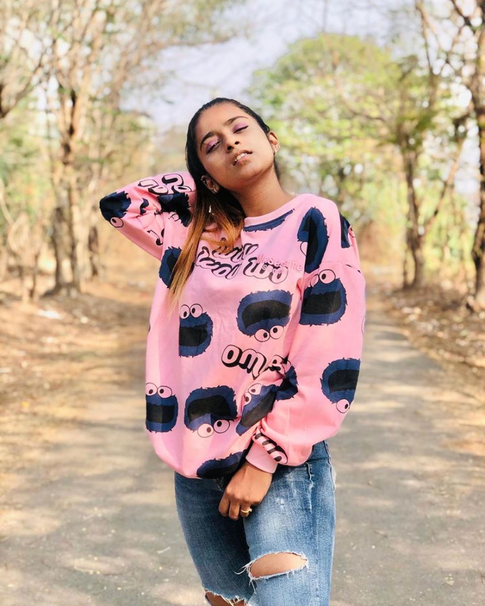 TikTok dancer/influencer Suhana Khan standing outside in a park wearing ripped blue jeans and a pink sweater with Cookie Monster on it