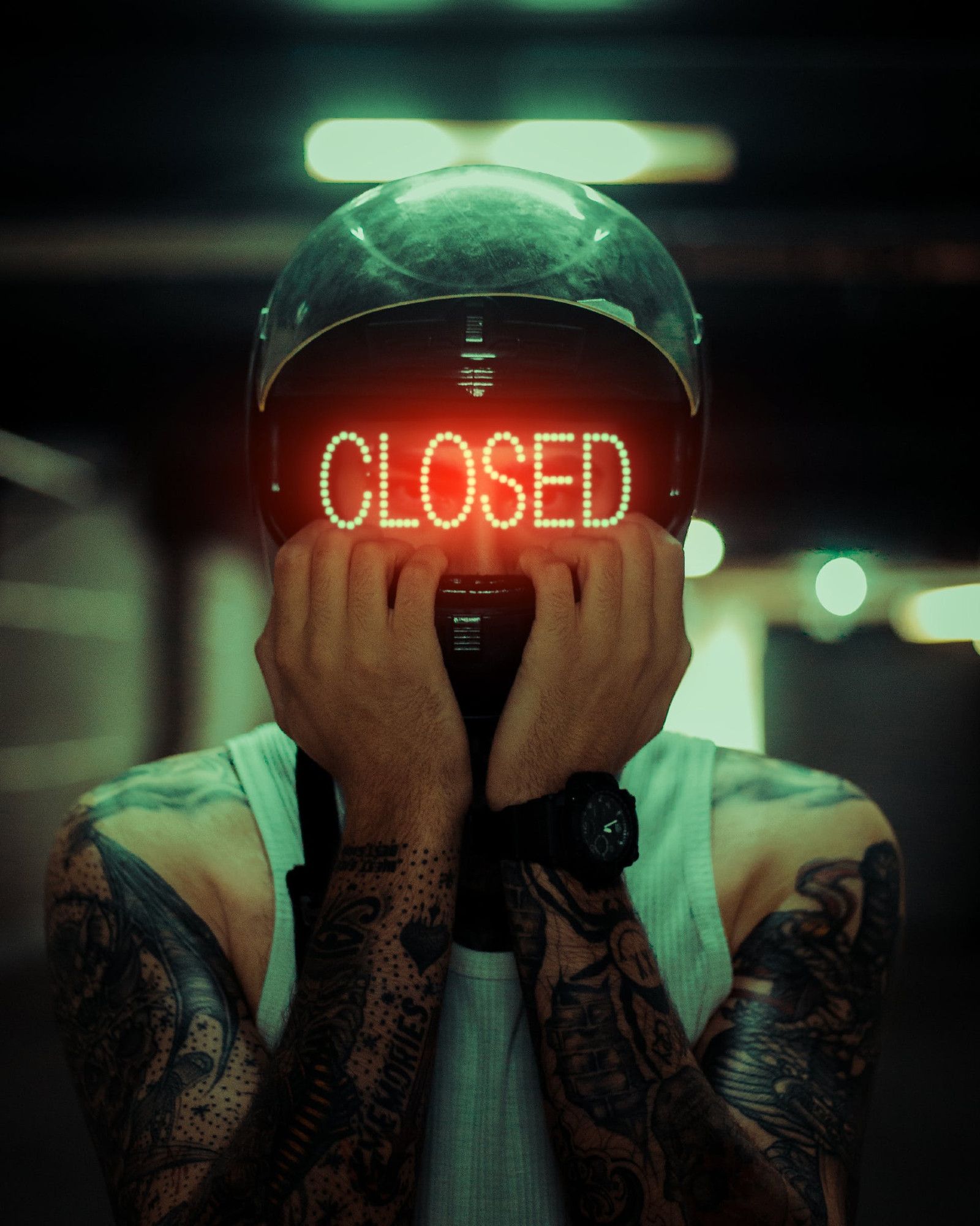 Tattooed man wearing motorcycle helmet with "CLOSED" in red digital letters where the face mask should be