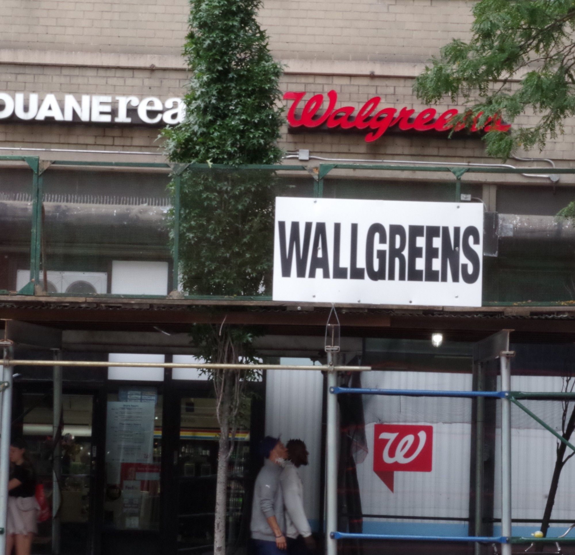 Photo of well-known NYC chain pharmacy with large temporary sign reading "WALLGREENS" directly in line with original "Walgreens" signage behind.