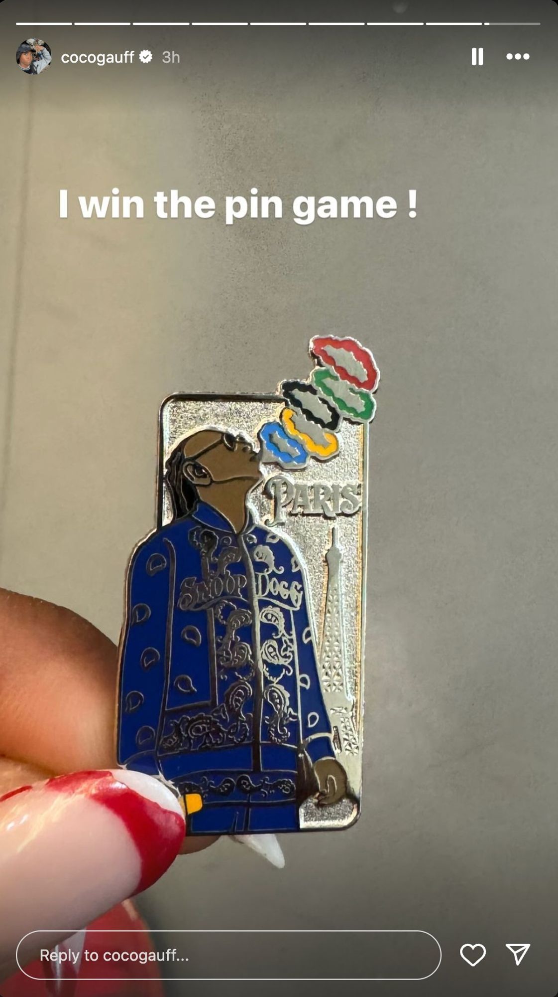 Screenshot from a Coco Gauff Instagram story.

Text: "I win the pin game!"

Photo: Fingers with red and white nail polish holding a pin that depicts Snoop Dogg in an ornate blue jacket with his name on the front blowing out five smoke rings colored like the Olympic rings, with the word Paris and the silhouette of the Eiffel Tower in the background