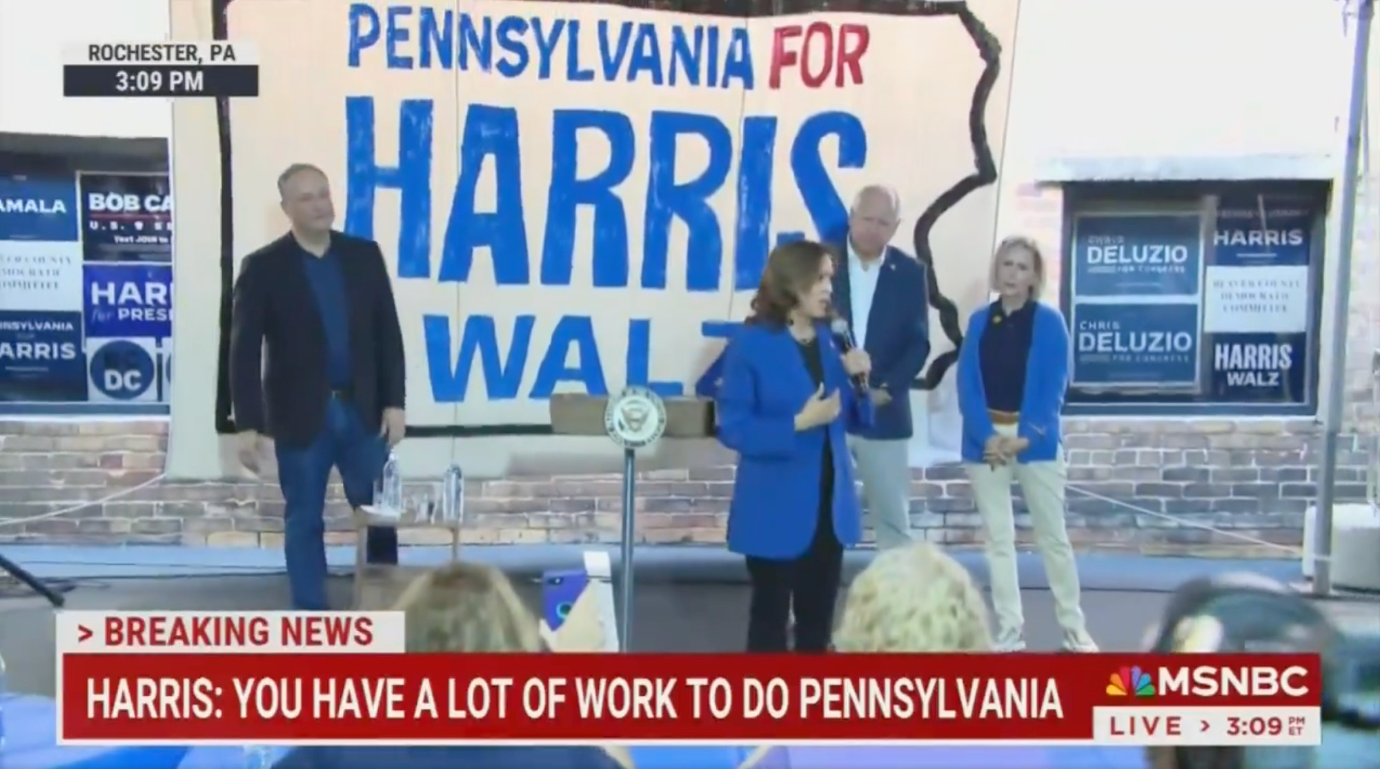 MSNBC video still of Kamala Harris walking around and speaking (no lectern) in front of what looks like a hand-painted "Pennsylvania for Harris-Walz" banner, with Doug Emhoff and Tim and Gwen Walz in the background