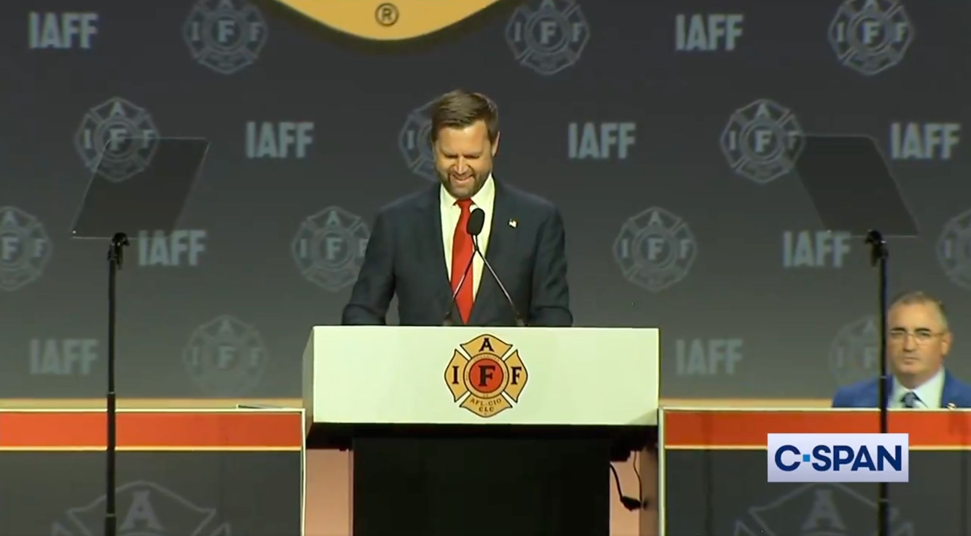 Screenshot of C-SPAN video of JD Vance at the lectern in the moment described above. Vance is looking down, half smiling, as he reacts to the boos.