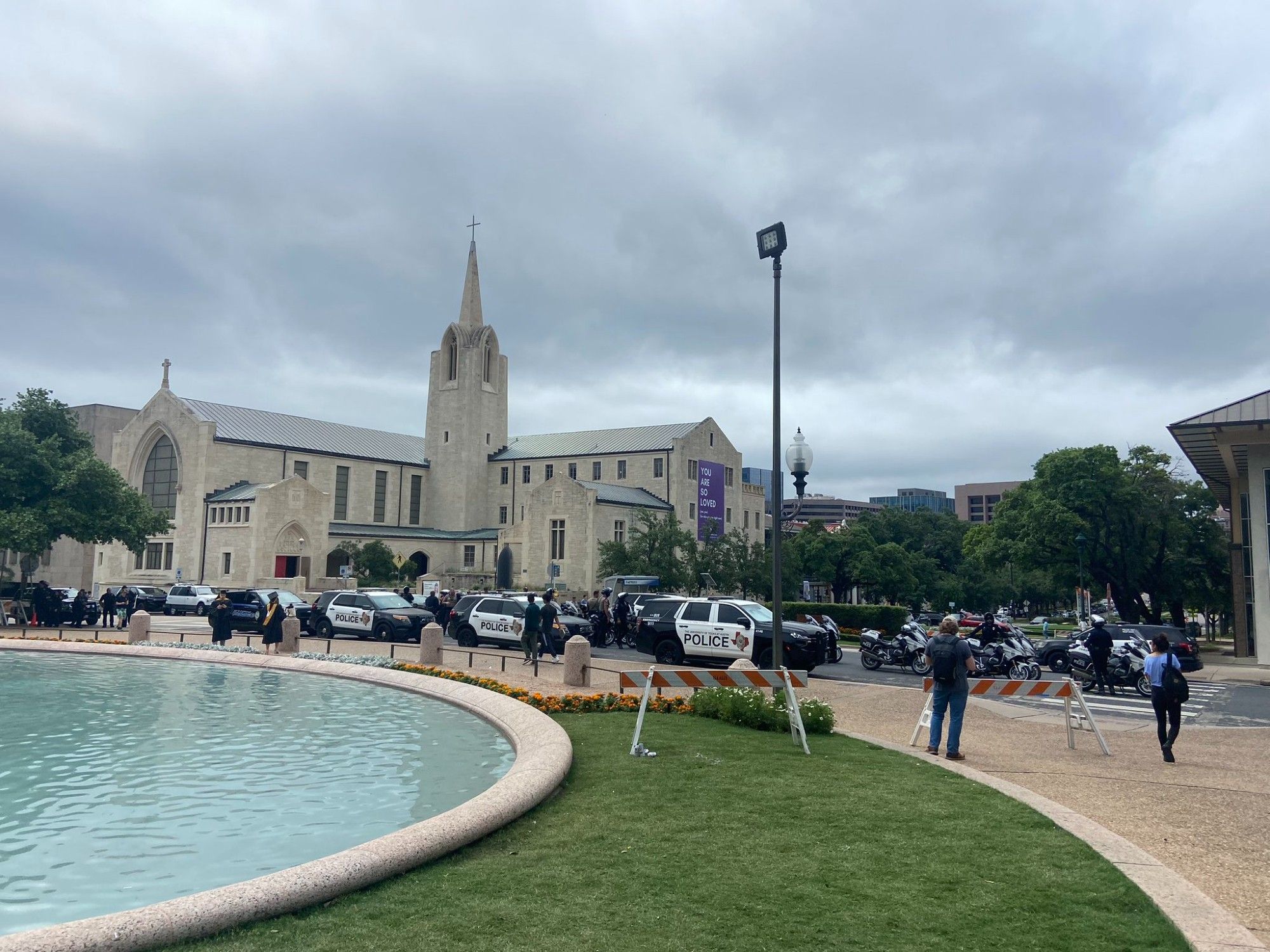 Police cars and motorcycles line a campus street next to the fountain at UT Austin in an otherwise peaceful scene