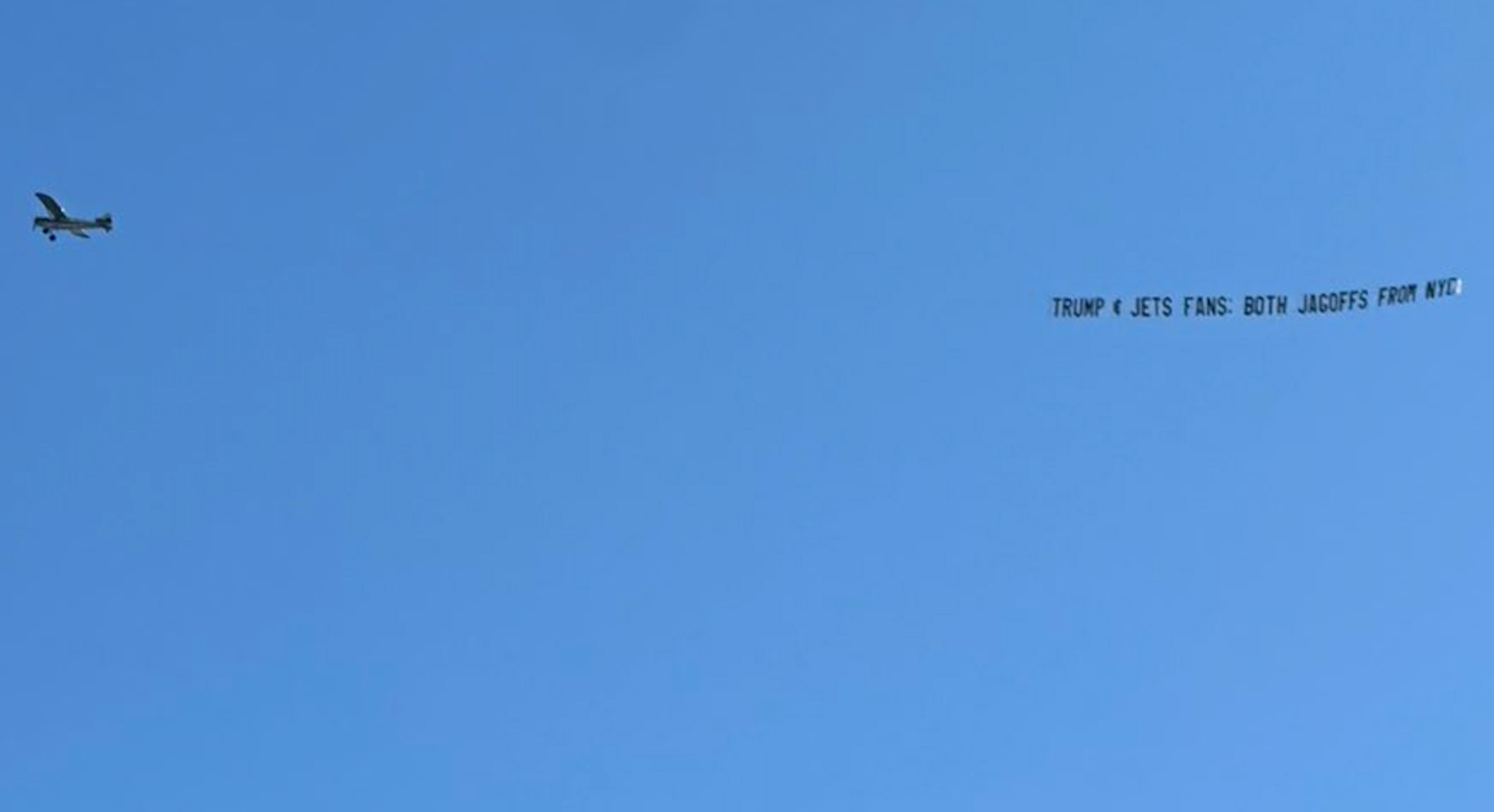 An airplane flies through the sky with a banner dangling behind it: TRUMP & JETS FANS: BOTH JAGOFFS FROM NYC