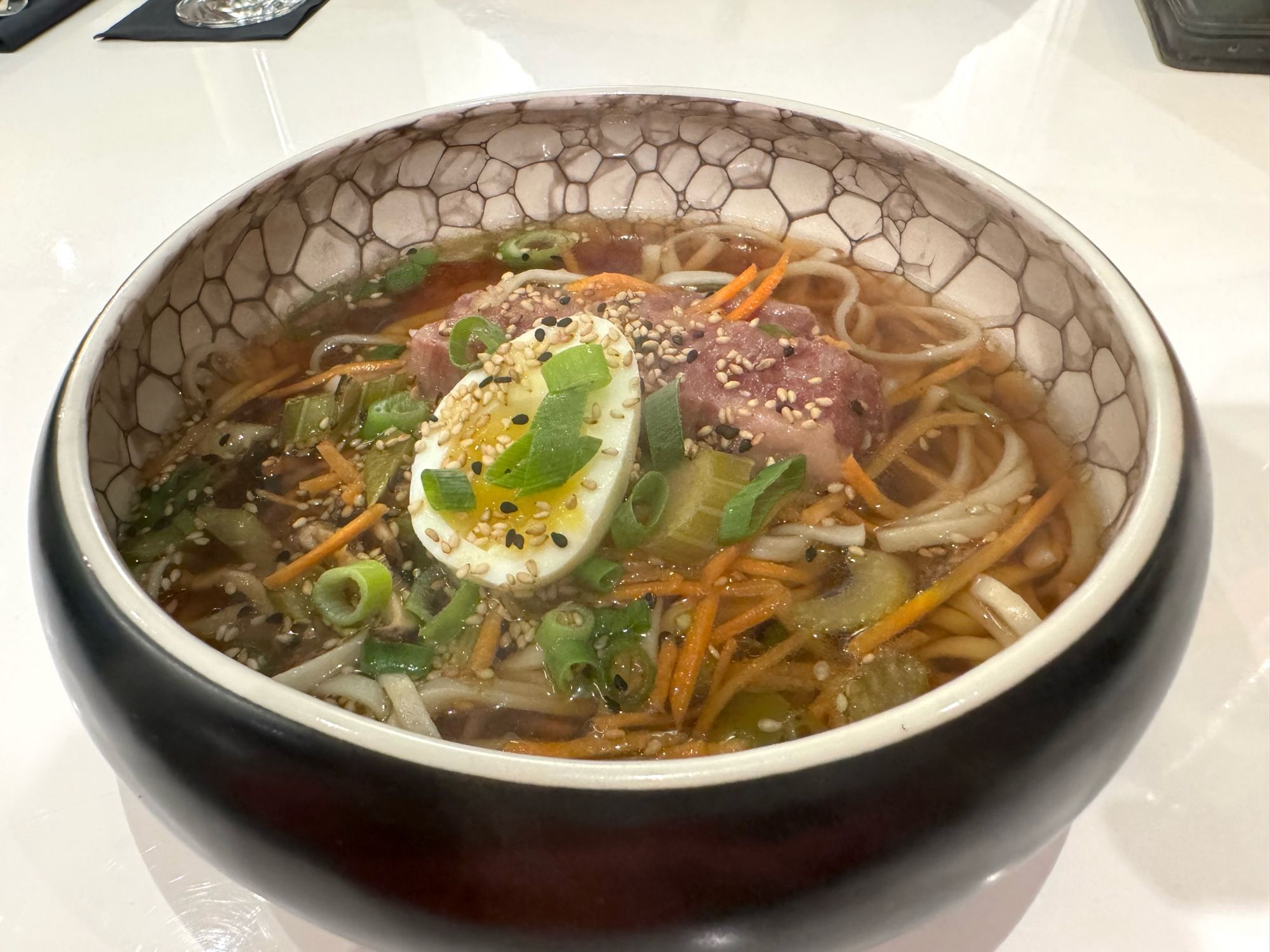 Ramen-Suppe mit Gemüse und halbem Ei in einer runden, innen marmorieren Schale.