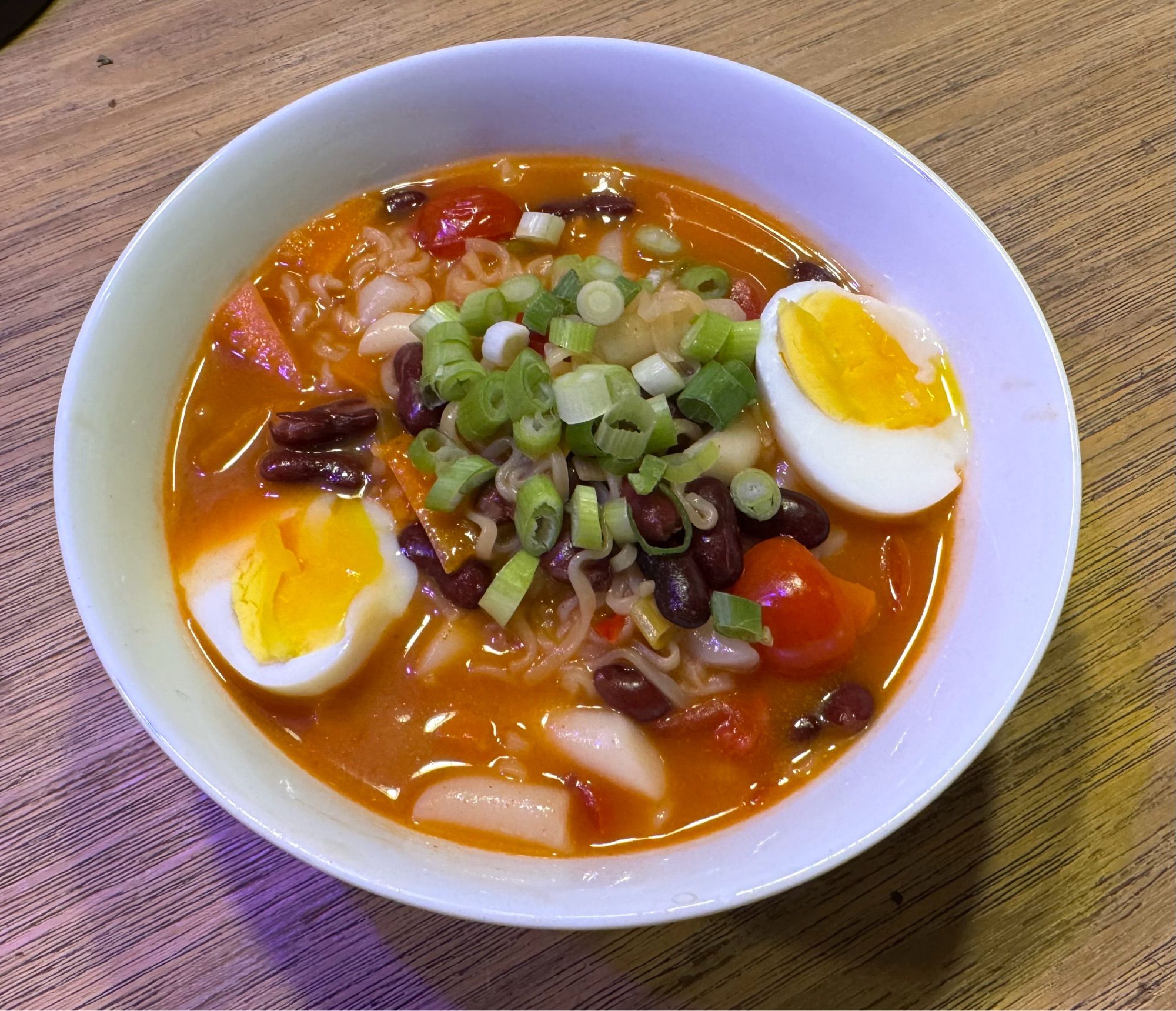 Weiße Schale mit roter Sauce, zwei Eierhälften, Frühlingszwiebeln obenauf. Die Reisküchlein sind vorne zu sehen.