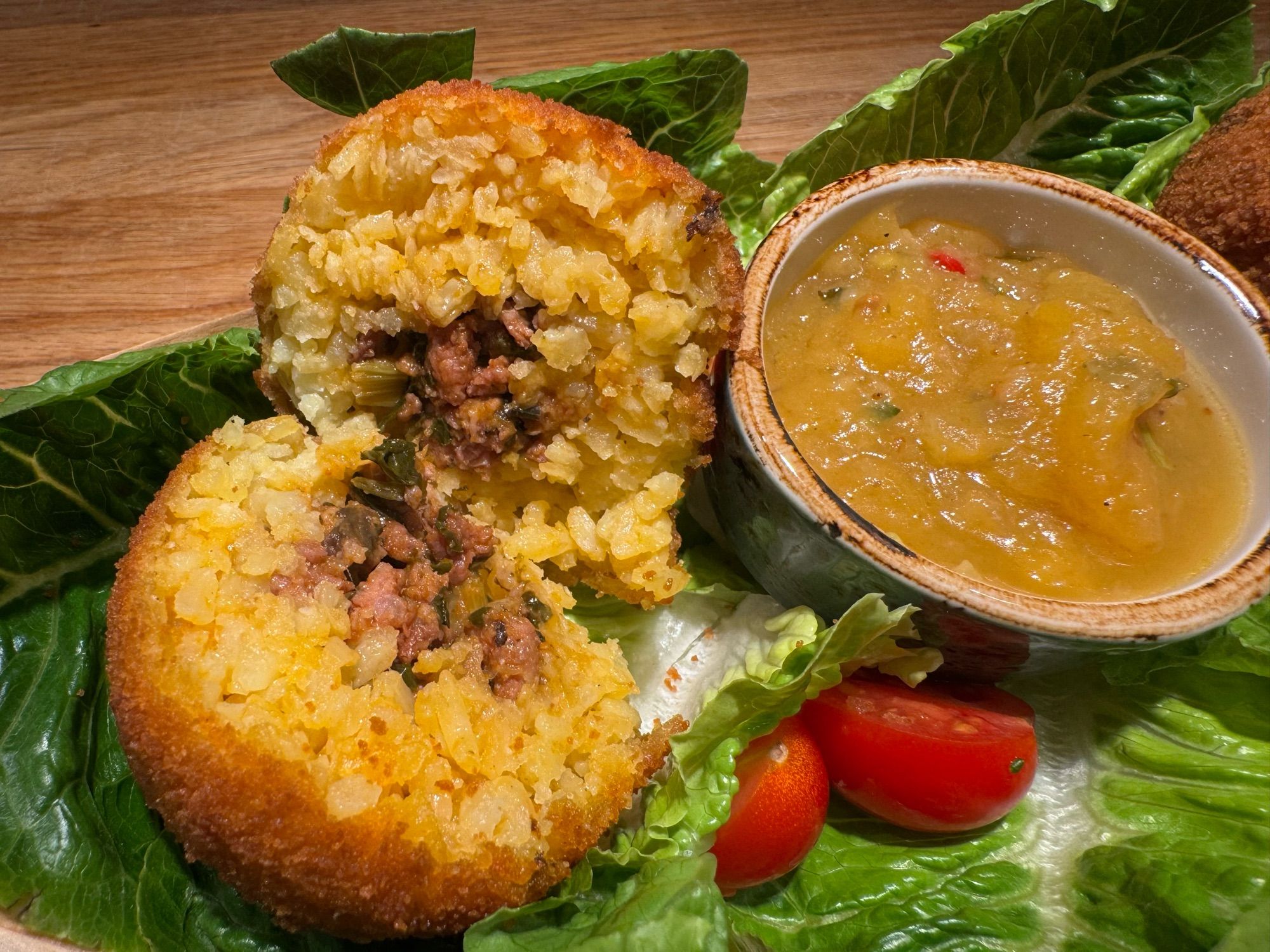 Nahaufnahme von einem aufgeschnittenen Arancini-Bällchen. Der Reis mit Safran umschließt die knusprig gebratene Pflanzenhack-Füllung mit Pinienkernen.