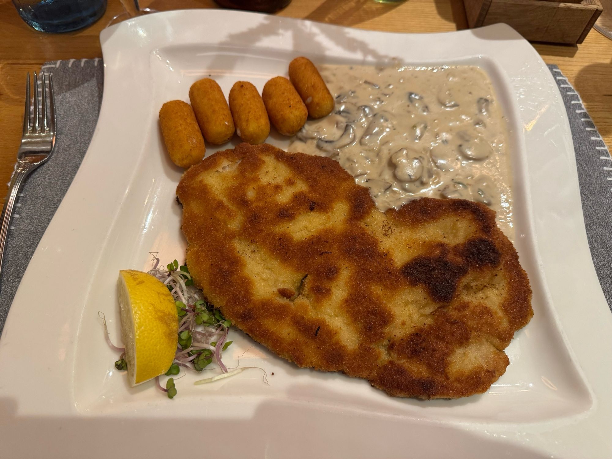 Grosses Dünenstraße Schnitzel, goldbraun, oben rechts Rahmpilz-Sauce, links fünf Kroketten.