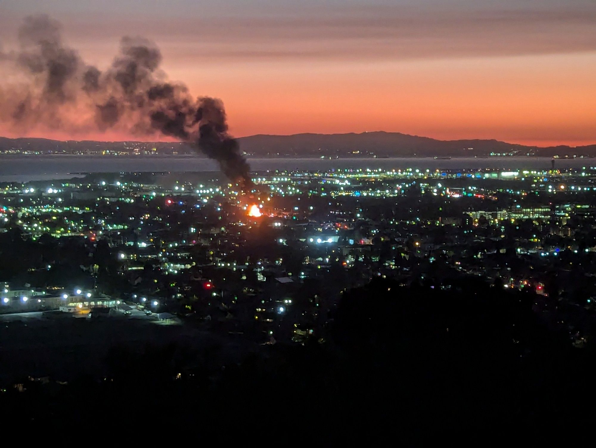 San Leandro from the eastern hills, just after sundown. There is a house fire in the middle of the frame and smoke blowing up to the left.