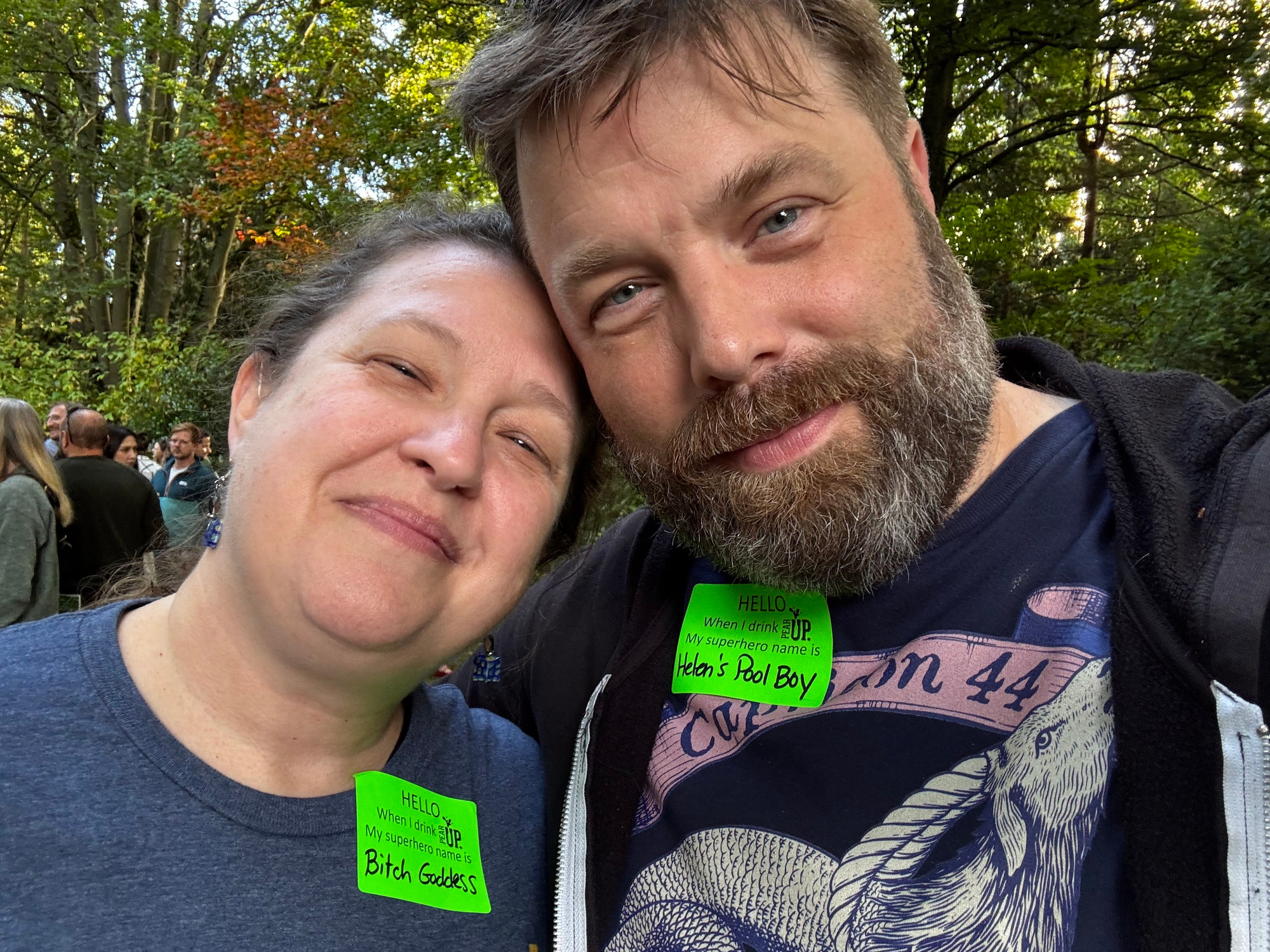 The poster and his partner, leaving together and smiling, each with superhero name tags. Hers Reid’s “bitch goddess “. his reads “Helen‘s pool boy. “