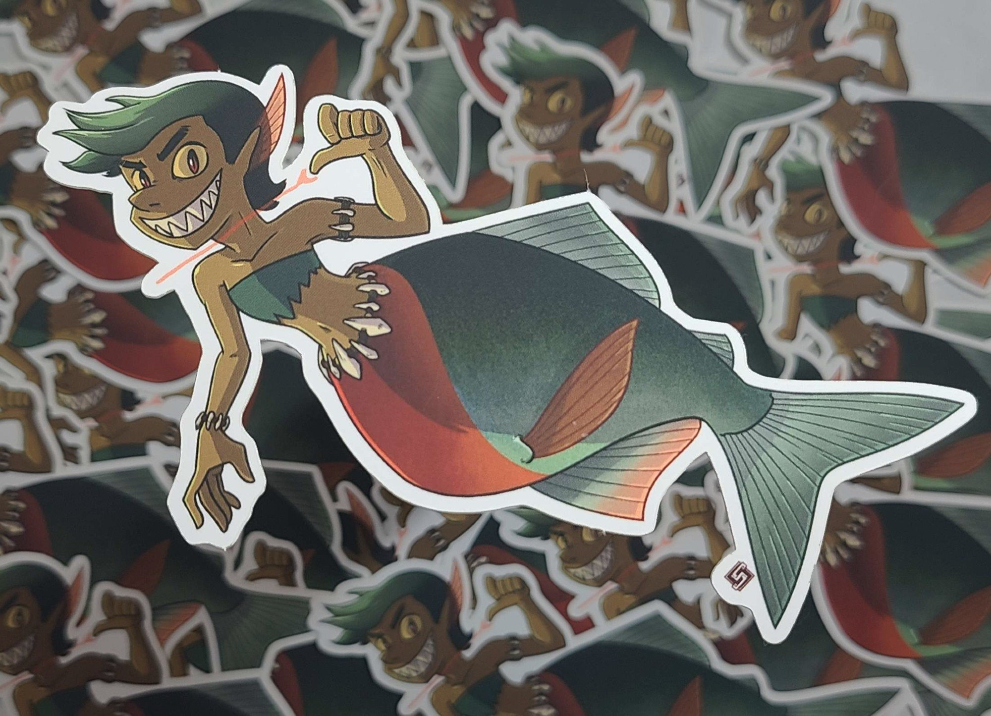 A sticker of a mermaid with a piranha tail. She has bone-themed jewelry and sharp teeth. She's drawing her thumb across her neck in a "you're next" kind of gesture.