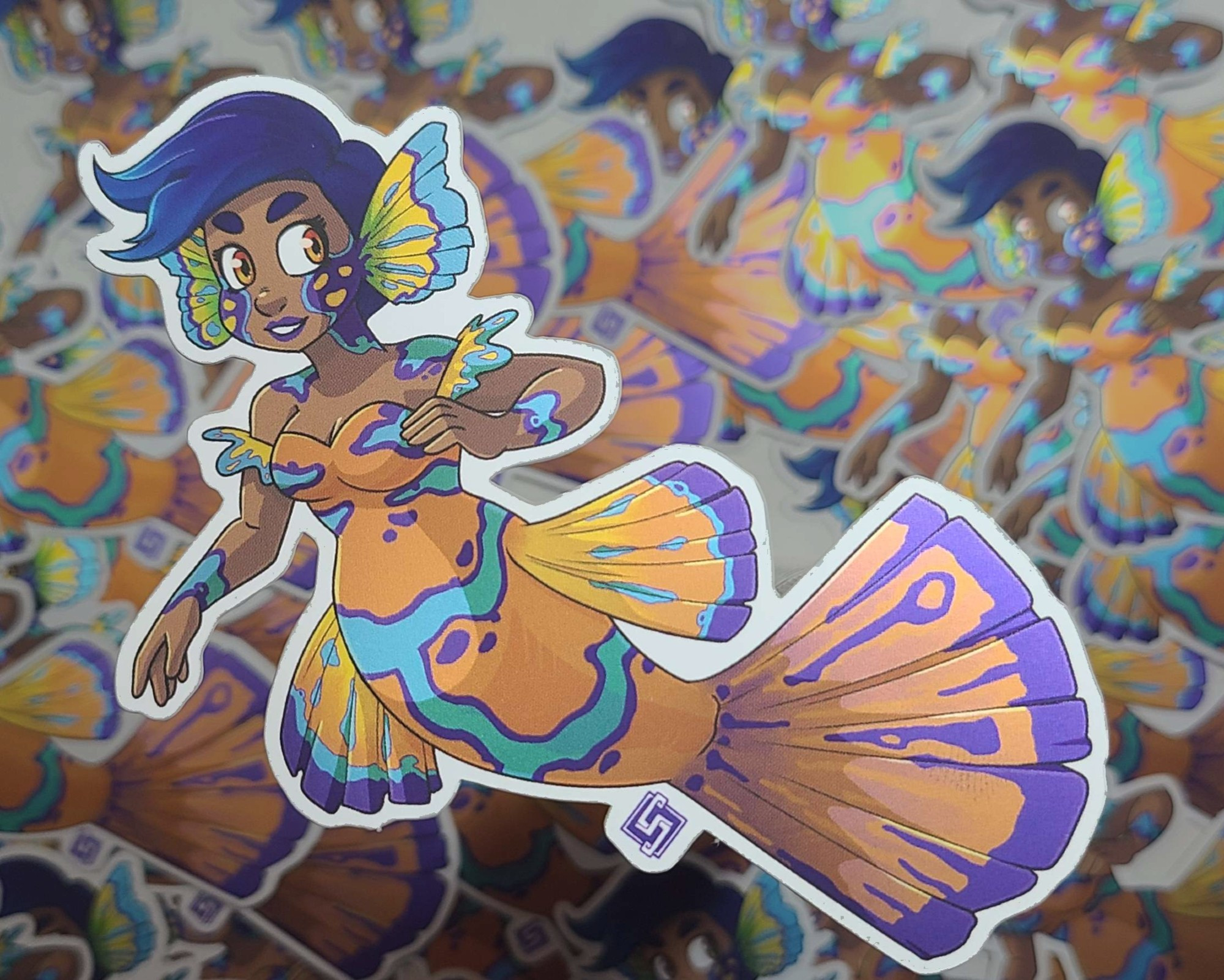 A sticker of a mandarinfish mermaid. She has a bright orange fish body and broad fins, with blue streaks all over.