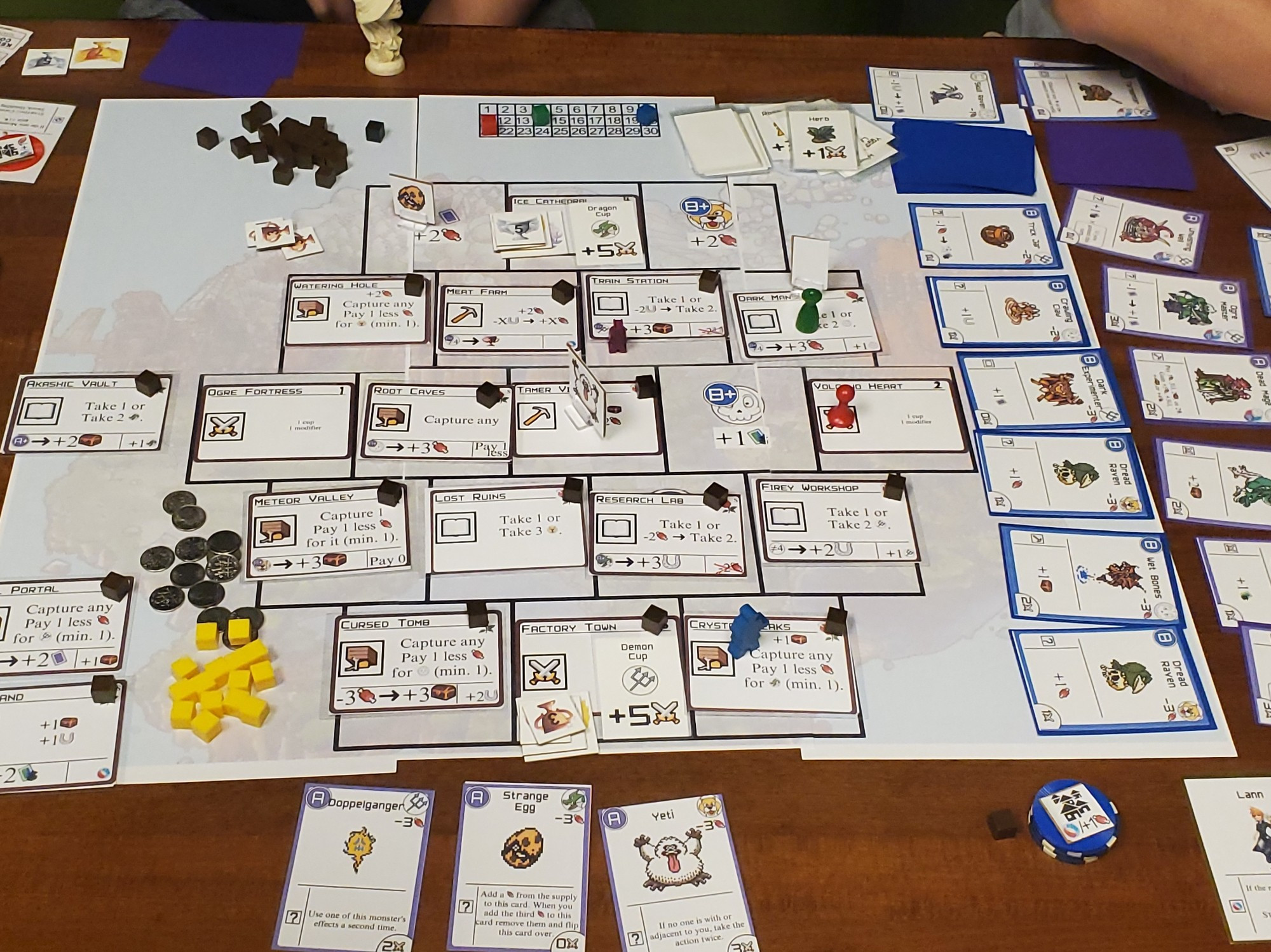 A board covered in cards. Off to the side are a dozen cards with pictures of monsters, and 3 more are at the bottom. To the left are piles of cubes.