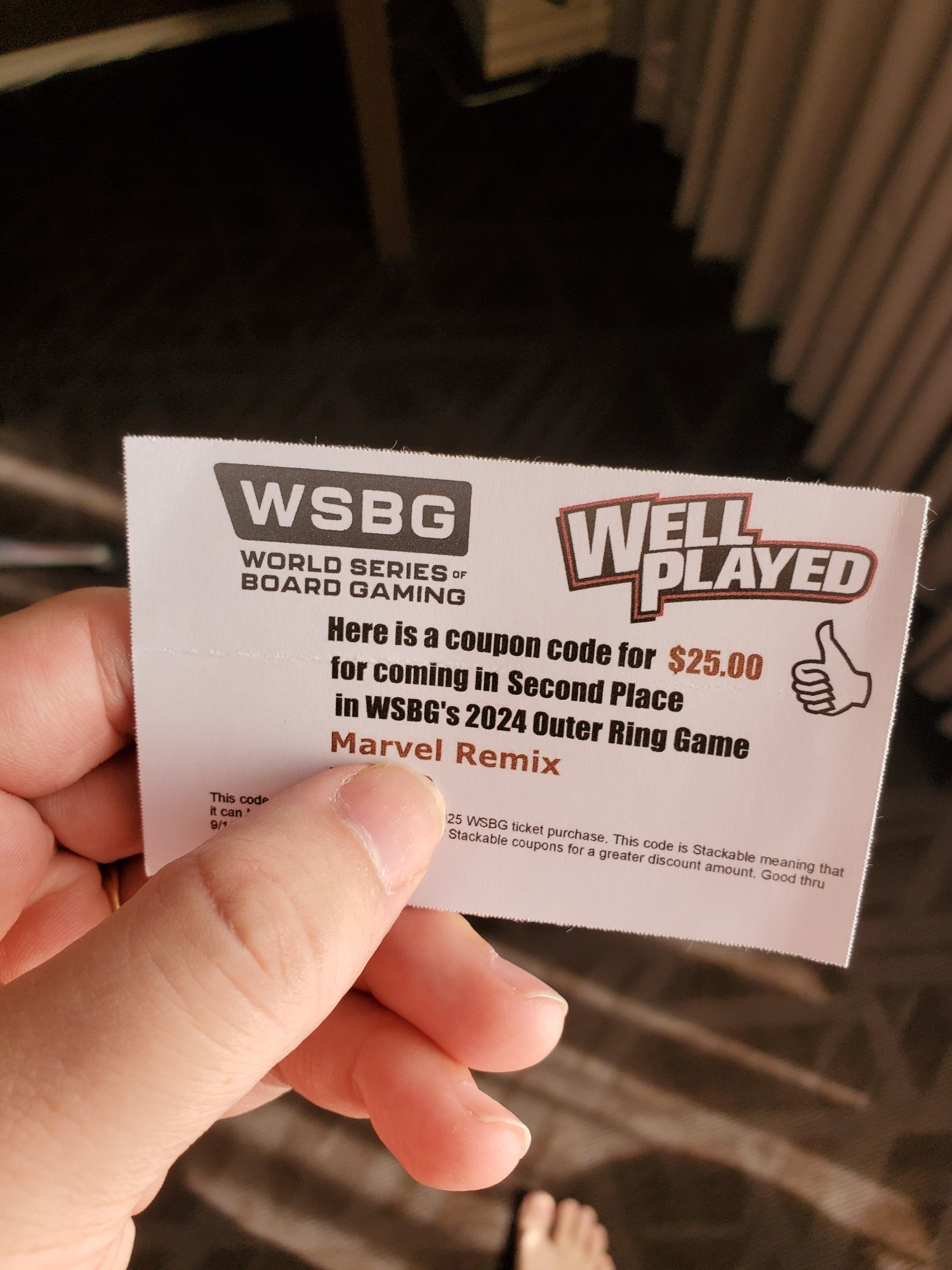 A hand holding a card which reads "WSBG World Series-Board Gaming, Well Played. Here is a coupon code for $25 for coming in Second Place in WSBG's 2024 Outer Ring Game for Marvel Remix."