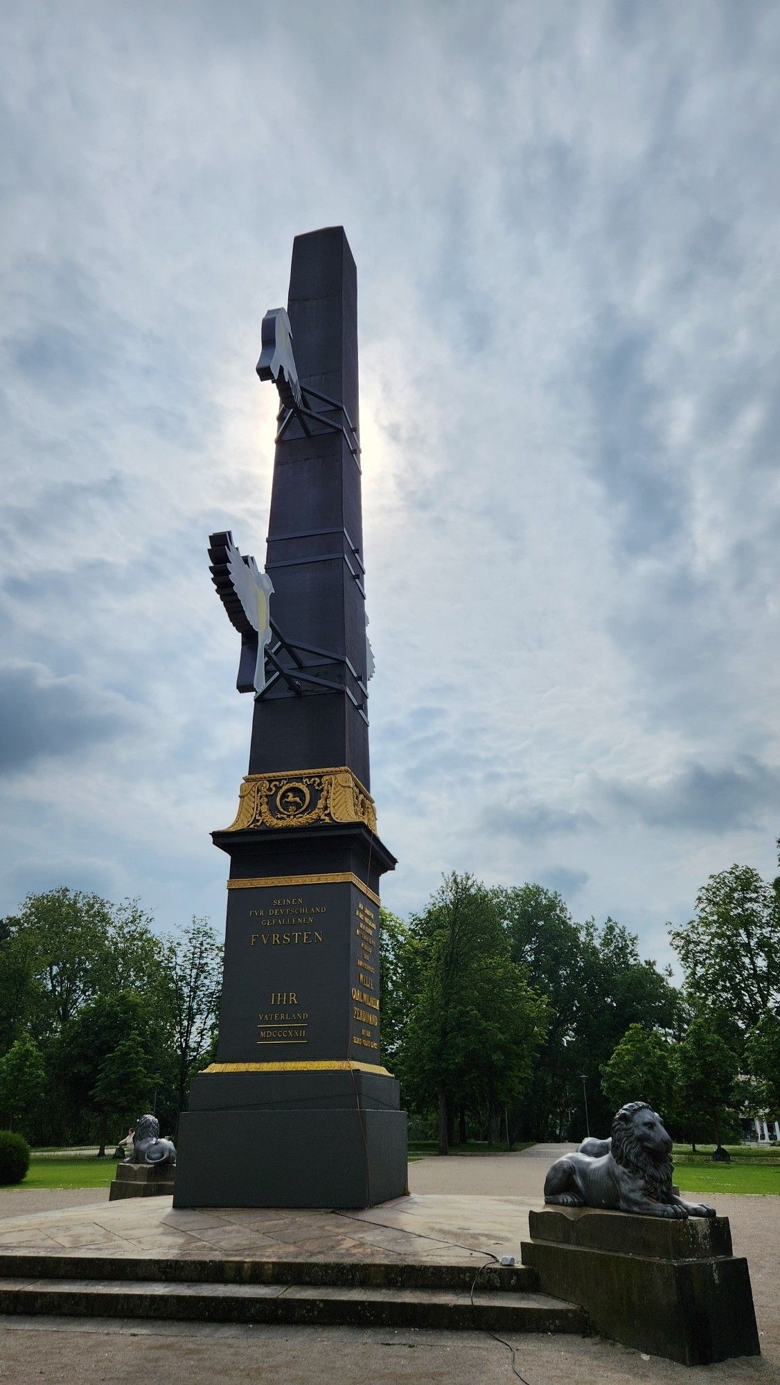 Foto des Obelisken auf dem Löwenwall mit einer Kunstinstallation des Lichtparcours 2024, das drei Meisen darstellt.