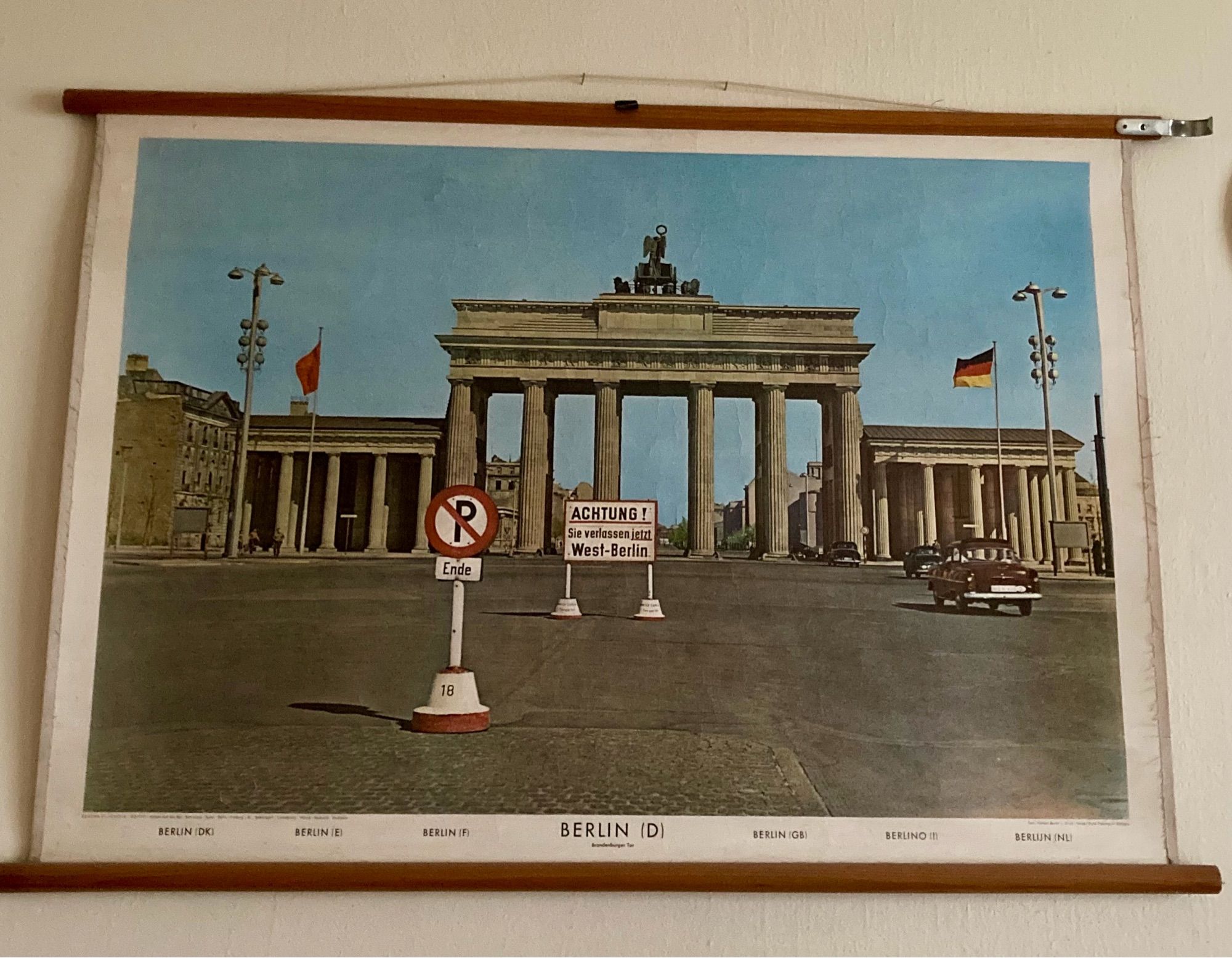 Eine alte Lehrtafel, ca aus den 60ern,  darauf das Brandenburger Tor mit einem schwarzen Auto und einem Schild „Achtung! Sie verlassen jetzt West-Berlin“