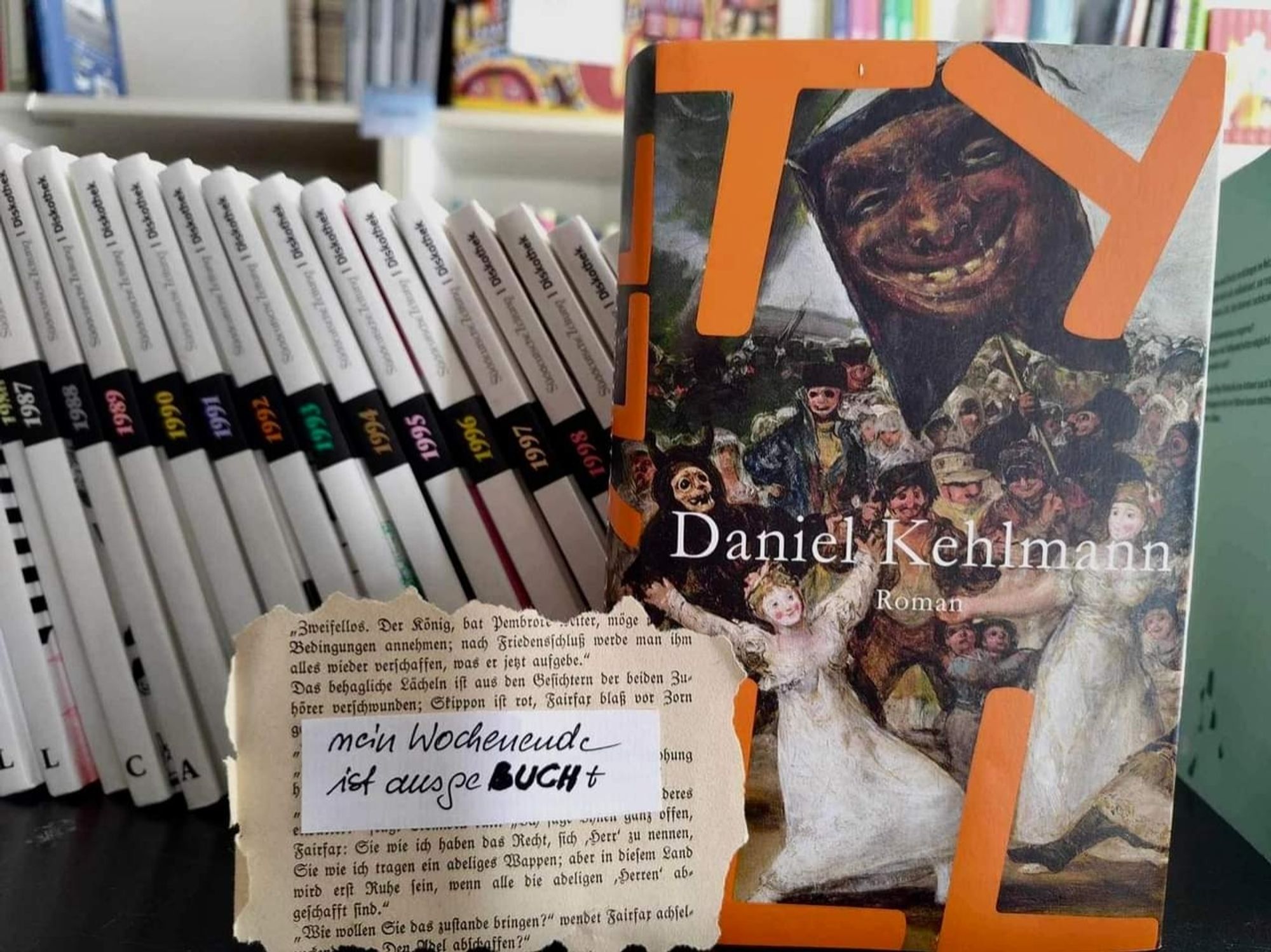 Man sieht das Buch Tyll von Daniel Kehlmann von vorne neben einer Buch-Kollektion mit weißen buchrücken. Davor steht ein Schild: Mein Wochenende ist ausgeBUCHT