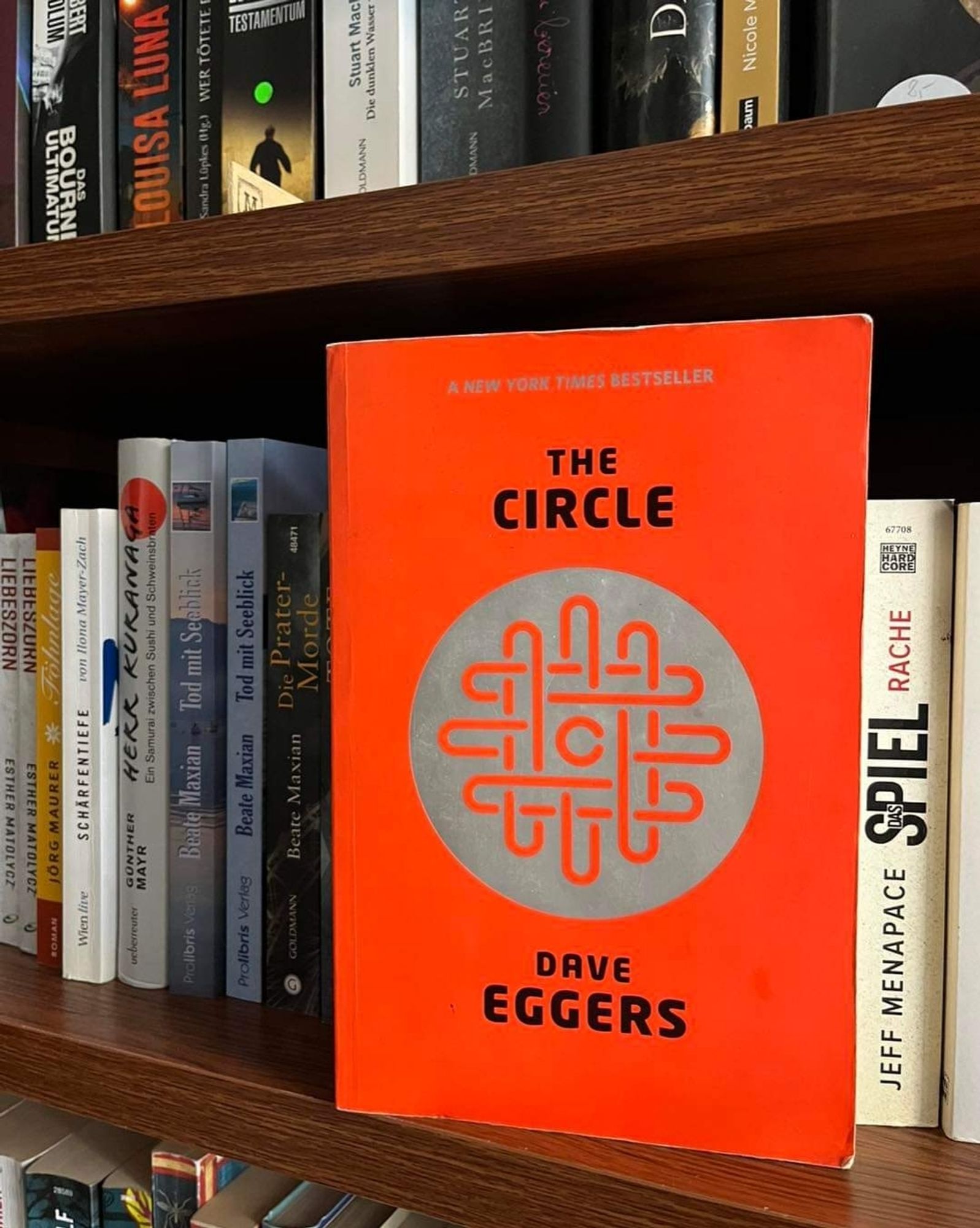 Das orangene Cover des Buches "The Circle" von Dave Eggers leuchtet aus einem Bücherregal hervor