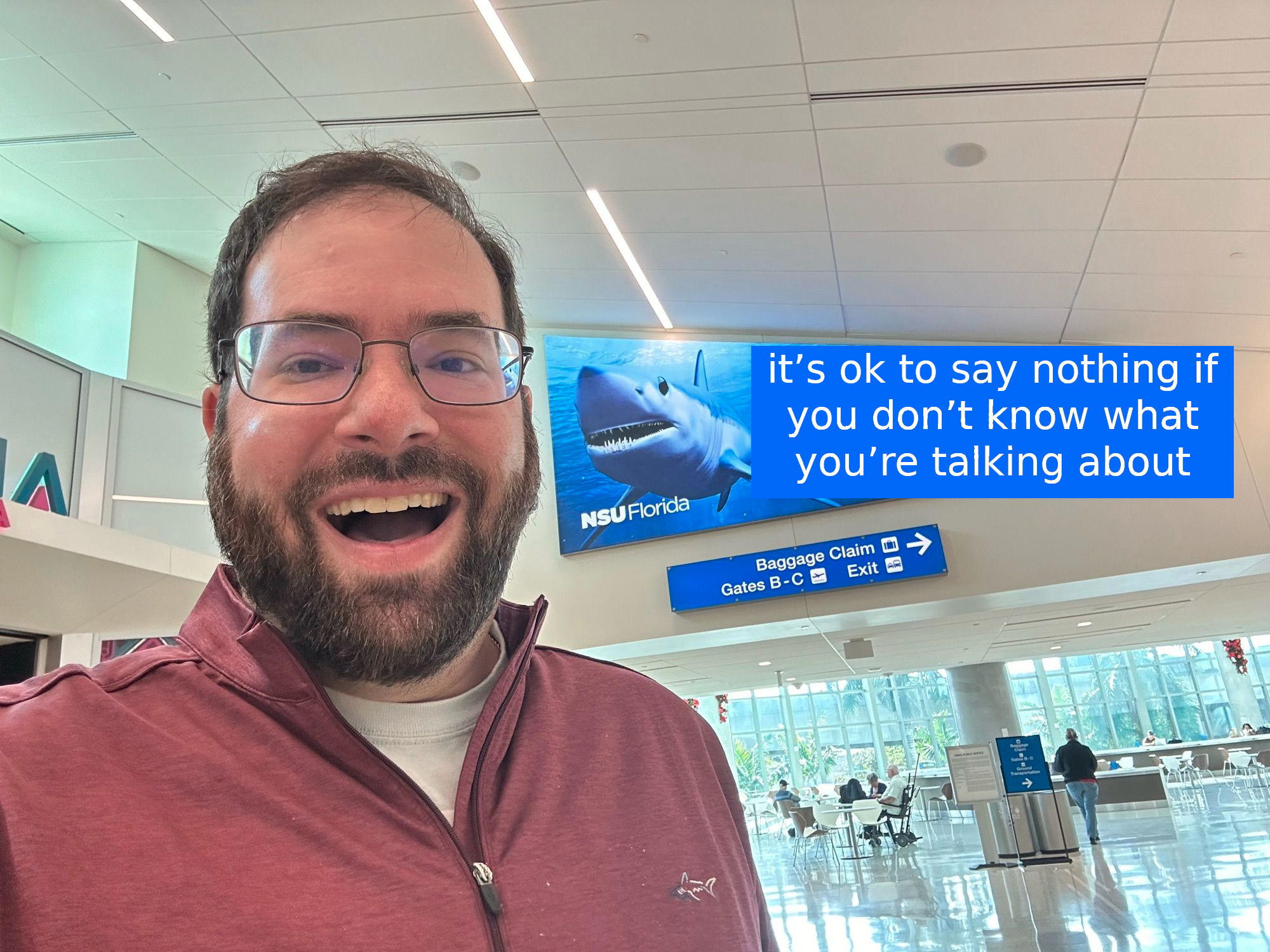 Man in front of a sign with a shark that says "it’s ok to say nothing if you don’t know what you’re talking about"