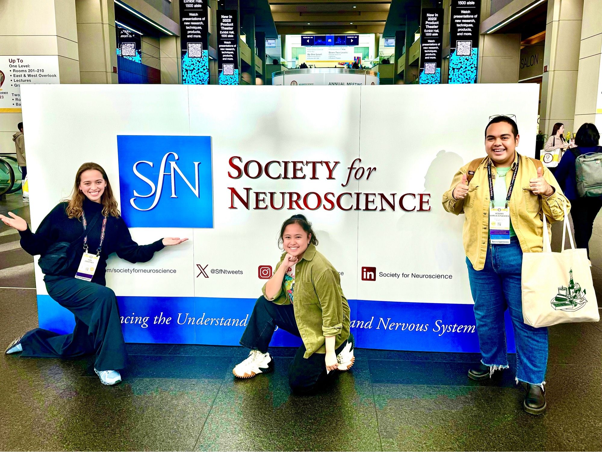 Three people in front of the society for neuroscience conference sign