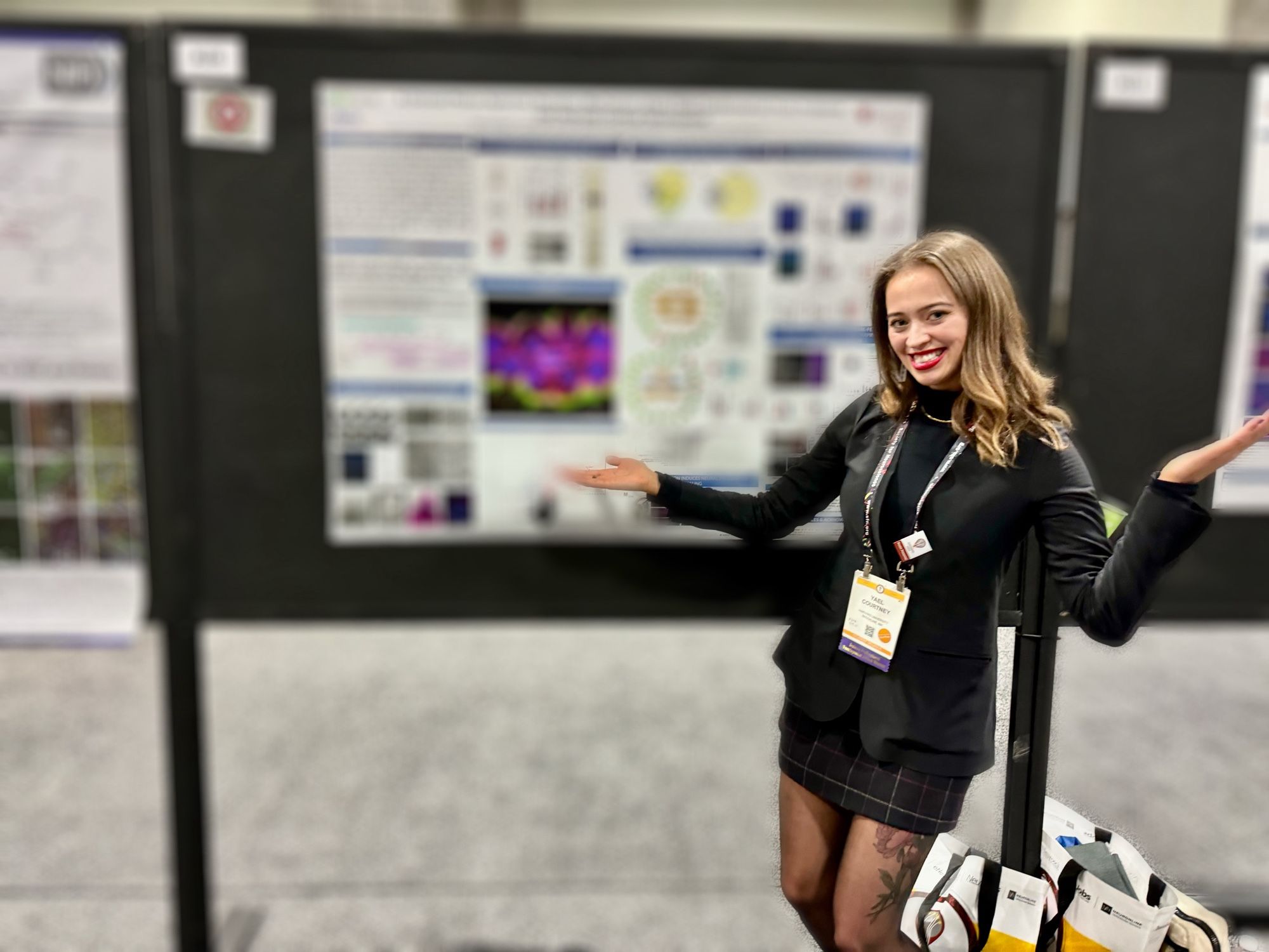 A girl smiling (me) in front of a blurred out scientific poster at the SfN annual meeting