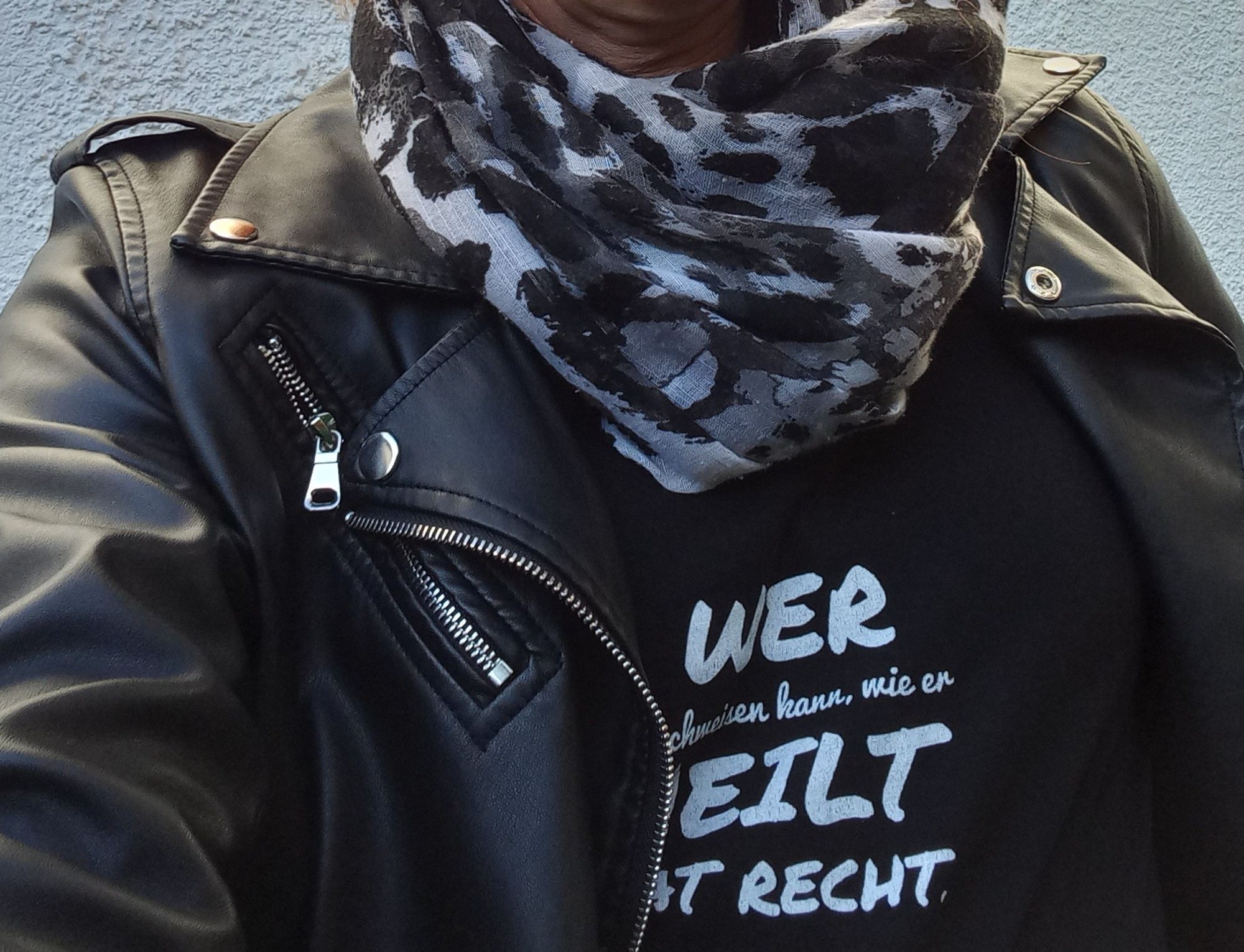 Ein Oberkörper bekleidet mit schwarzer Bikerjacke und schwarzem T-Shirt.  Aufdruck auf dem T-Shirt:Wer nachweisen kann wie er heilt hat Recht.