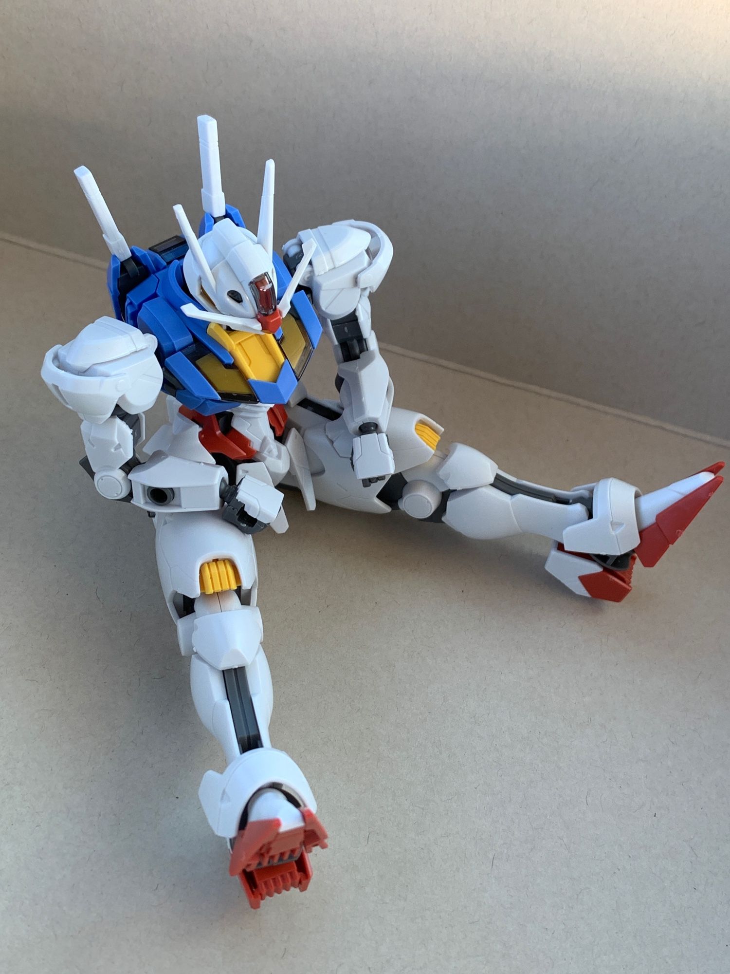 The HGWFM Gundam Aerial sitting on the floor with the legs straight out, her forearms resting on her thighs with the hands dangling limply, and head looking down, appearing depressed