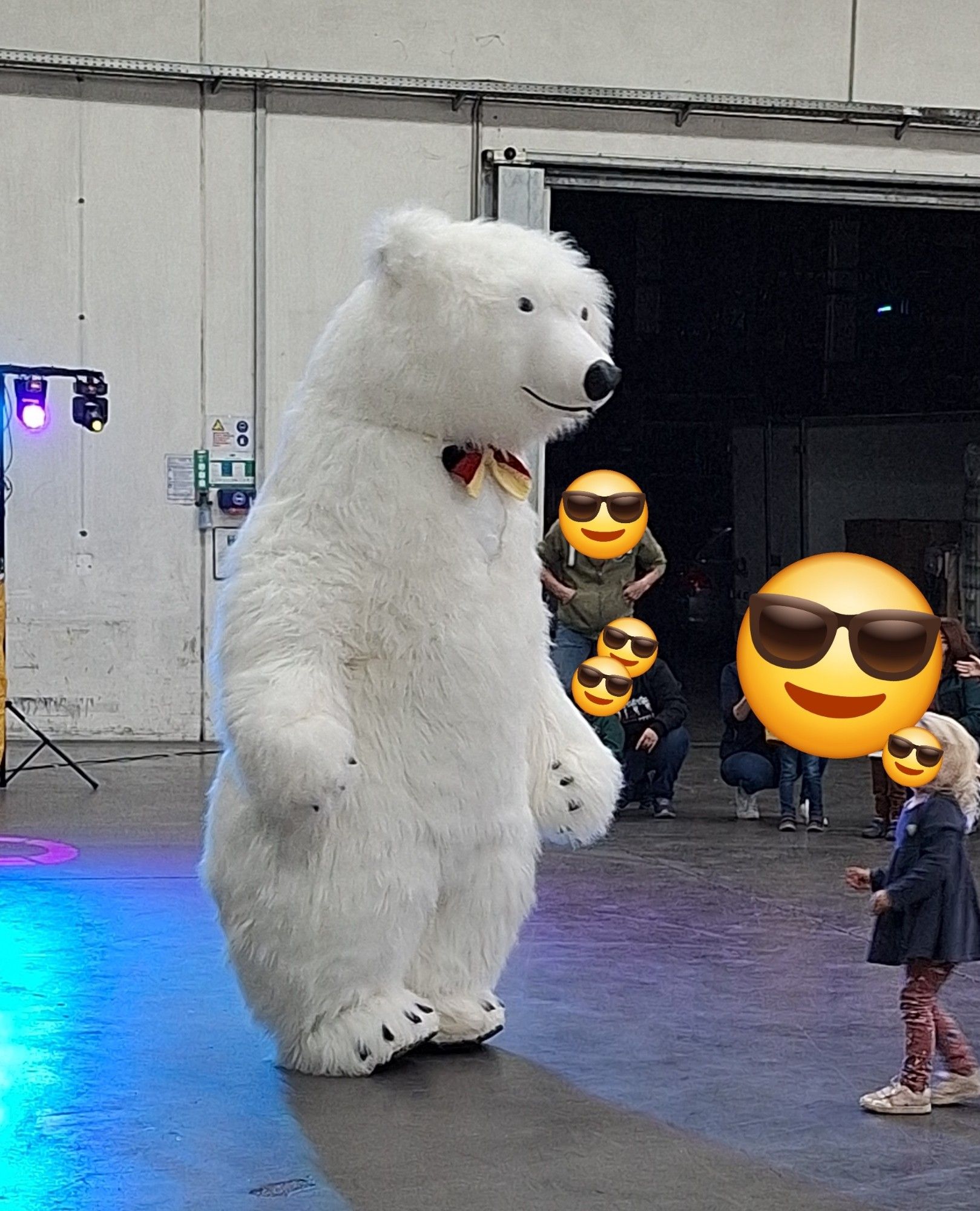 Person im Eisbärkostüm mit Fliege in schwarz/rot/gold tanzt vor ein paar Kindern.