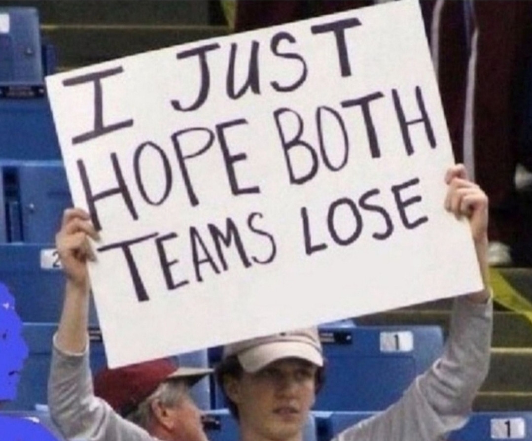 Ein Typ steht auf einer Tribüne und hält ein Schild hoch, auf dem steht: "I just hope both teams lose."