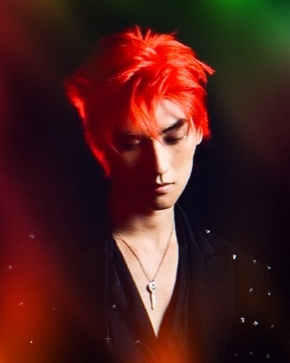 Huang Junjie with red hair and a black suit on a dark background