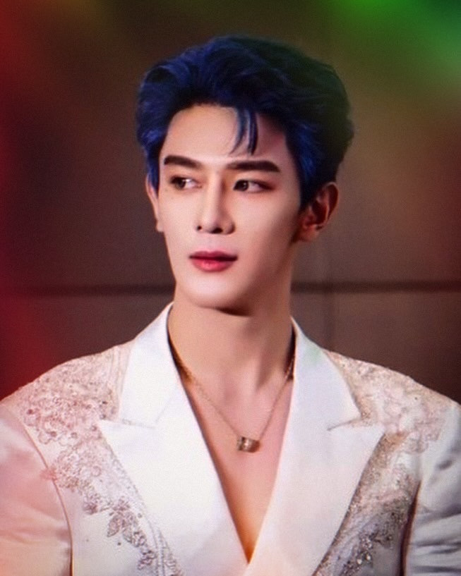 Xia Zhiguang with blue hair and a white suit on a light background