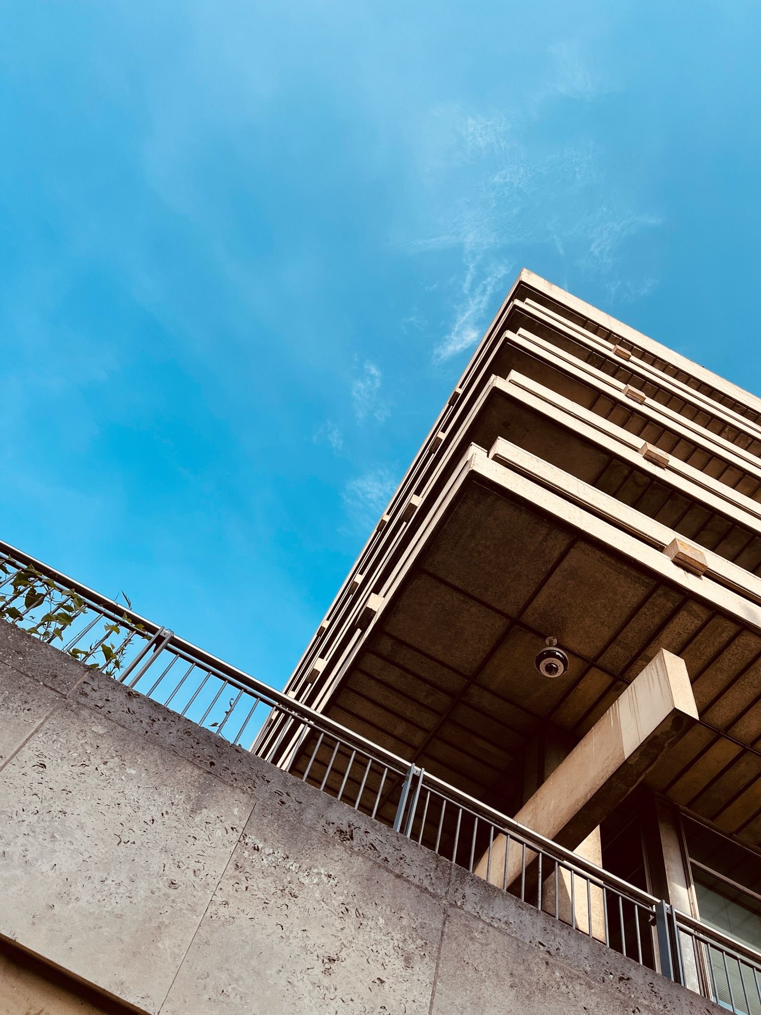 Photo looking up at the sky and up at a sharp corner of a concrete building with a concrete wall and metal railing running along the bottom