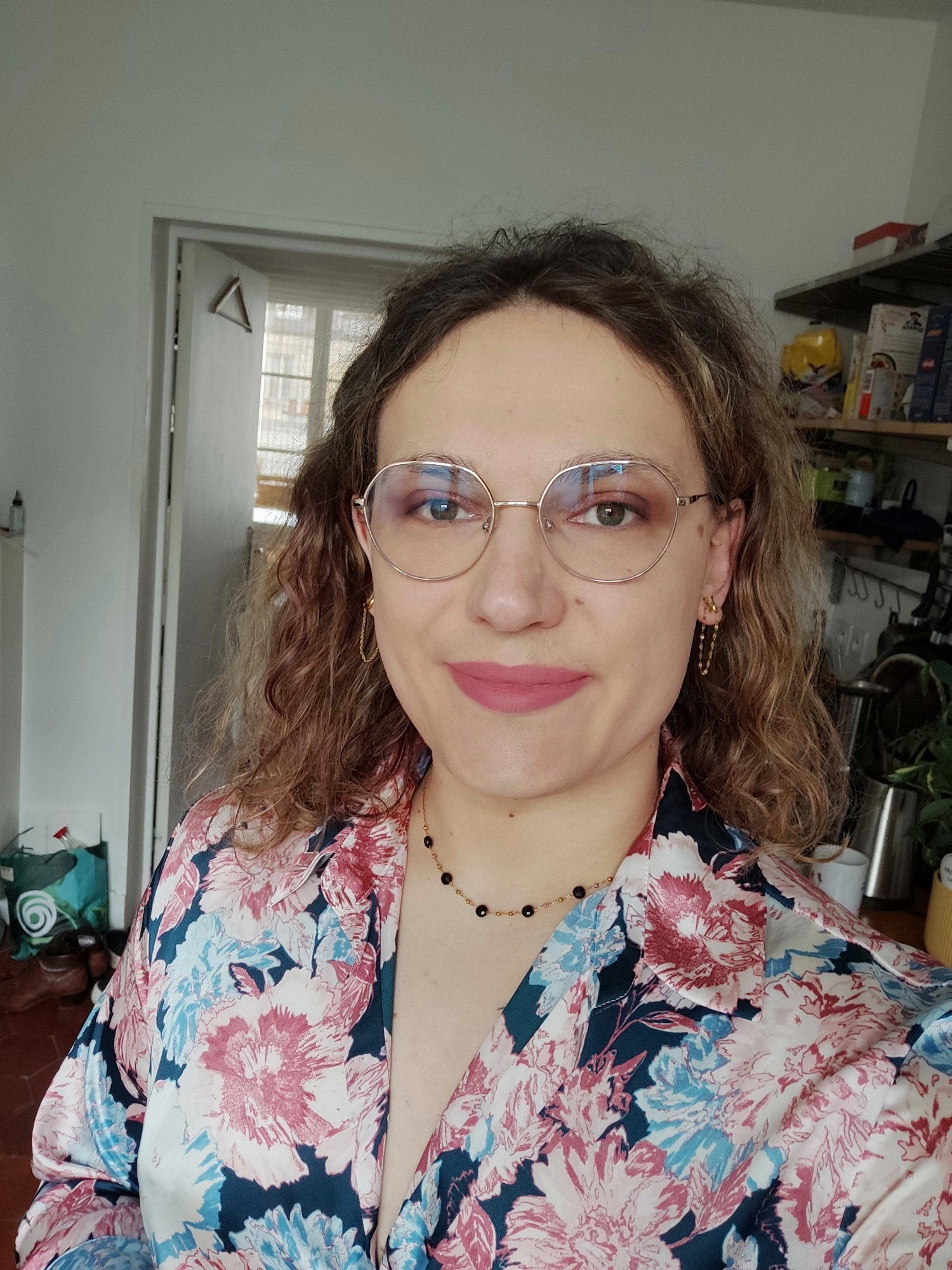 Selfie with my then new glasses, a very lesbian shirt with flowers on it, and a black and gold necklace