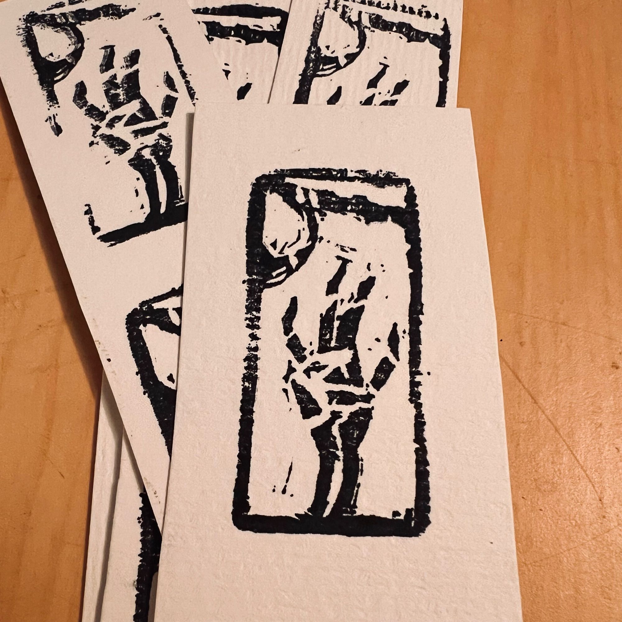 Photograph of a stack of simple prints on toothy paper of a skeletal hand reaching for a flute with a tassel hanging from it. The print is in a long, rectangular shape in black and white.