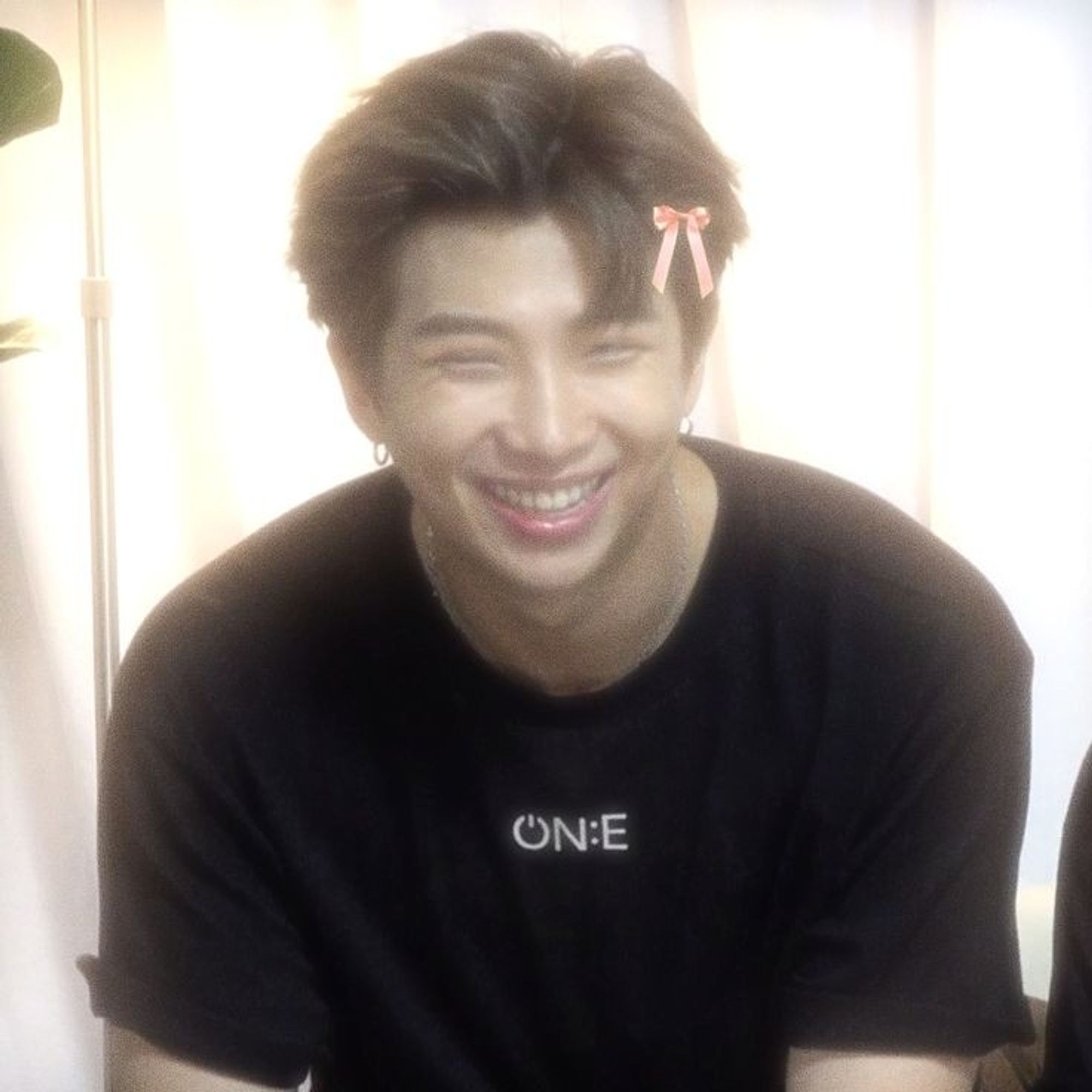 Kim Namjoon is smiling with a pink bow on his head.