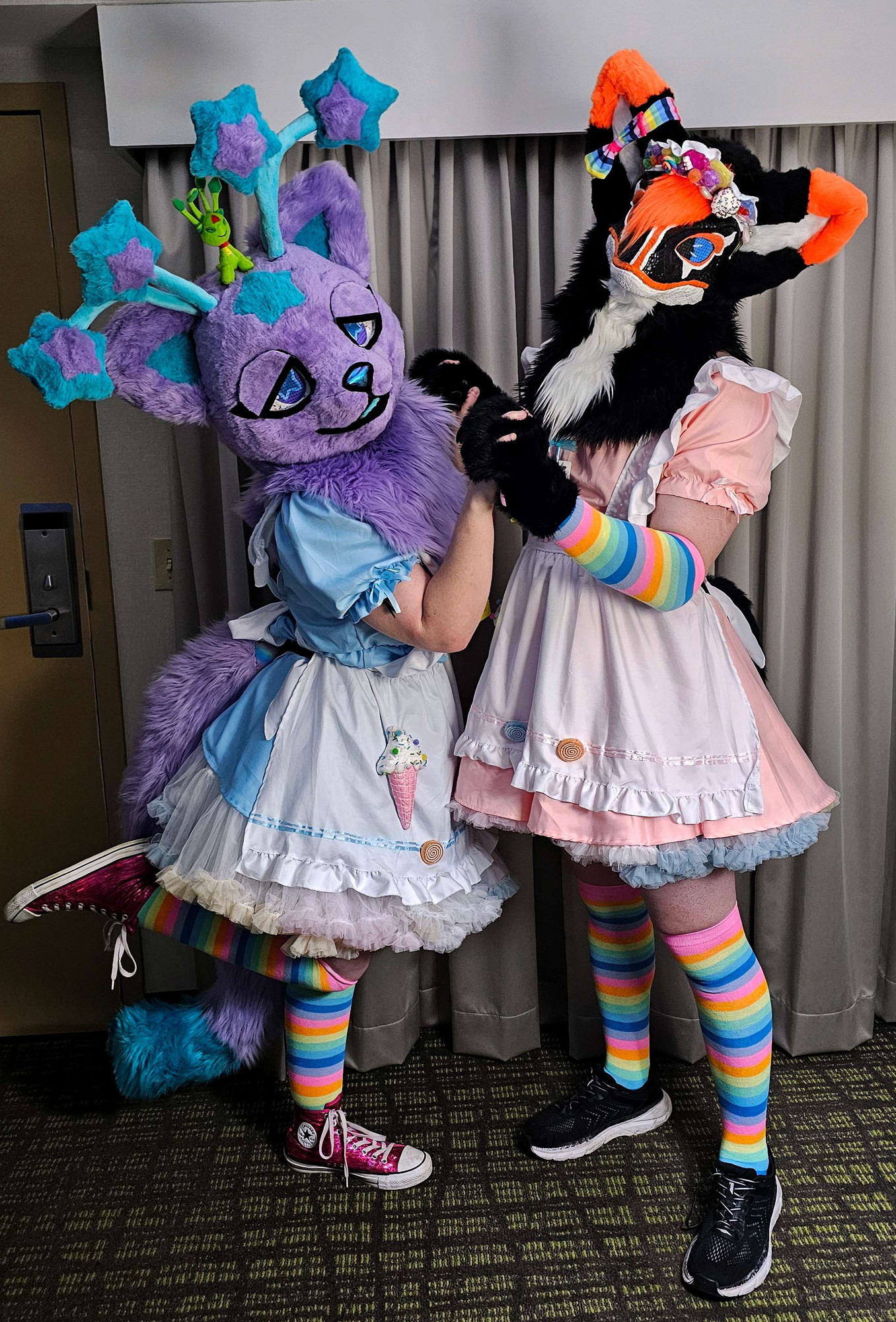 Purple alien cat fursuiter (Nova) and fox-raptor fursuiter (Fexy) in matching candy themed maid outfits holding hands