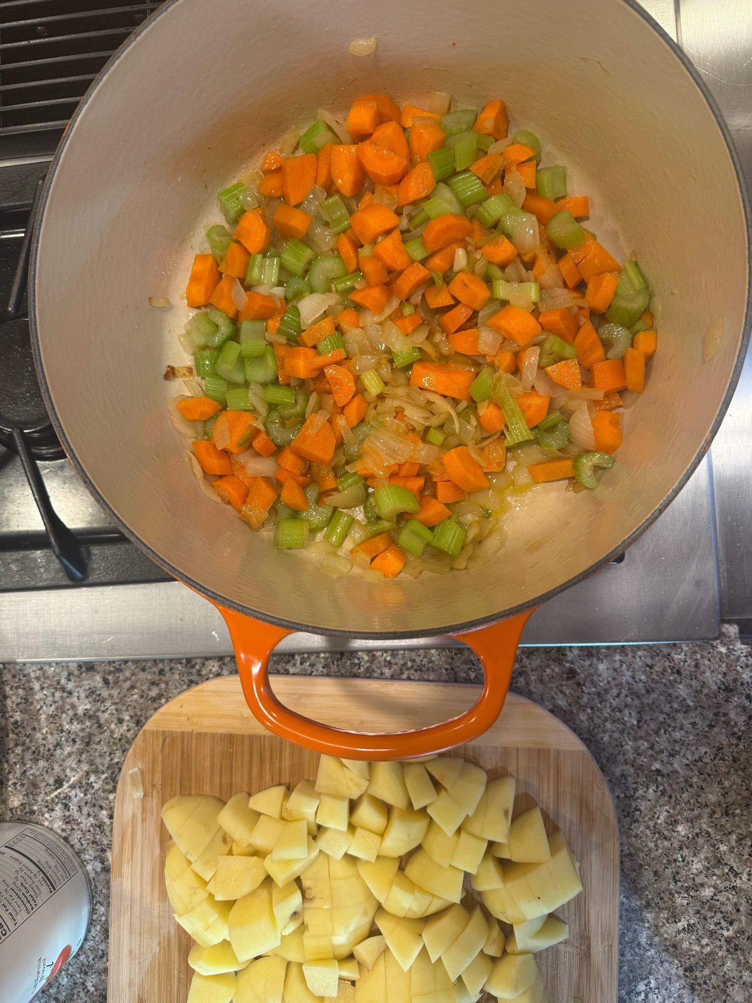 A big pot of diced carrots, onion, and celery.  Beside it on a cutting board is a pile of diced potatoes.