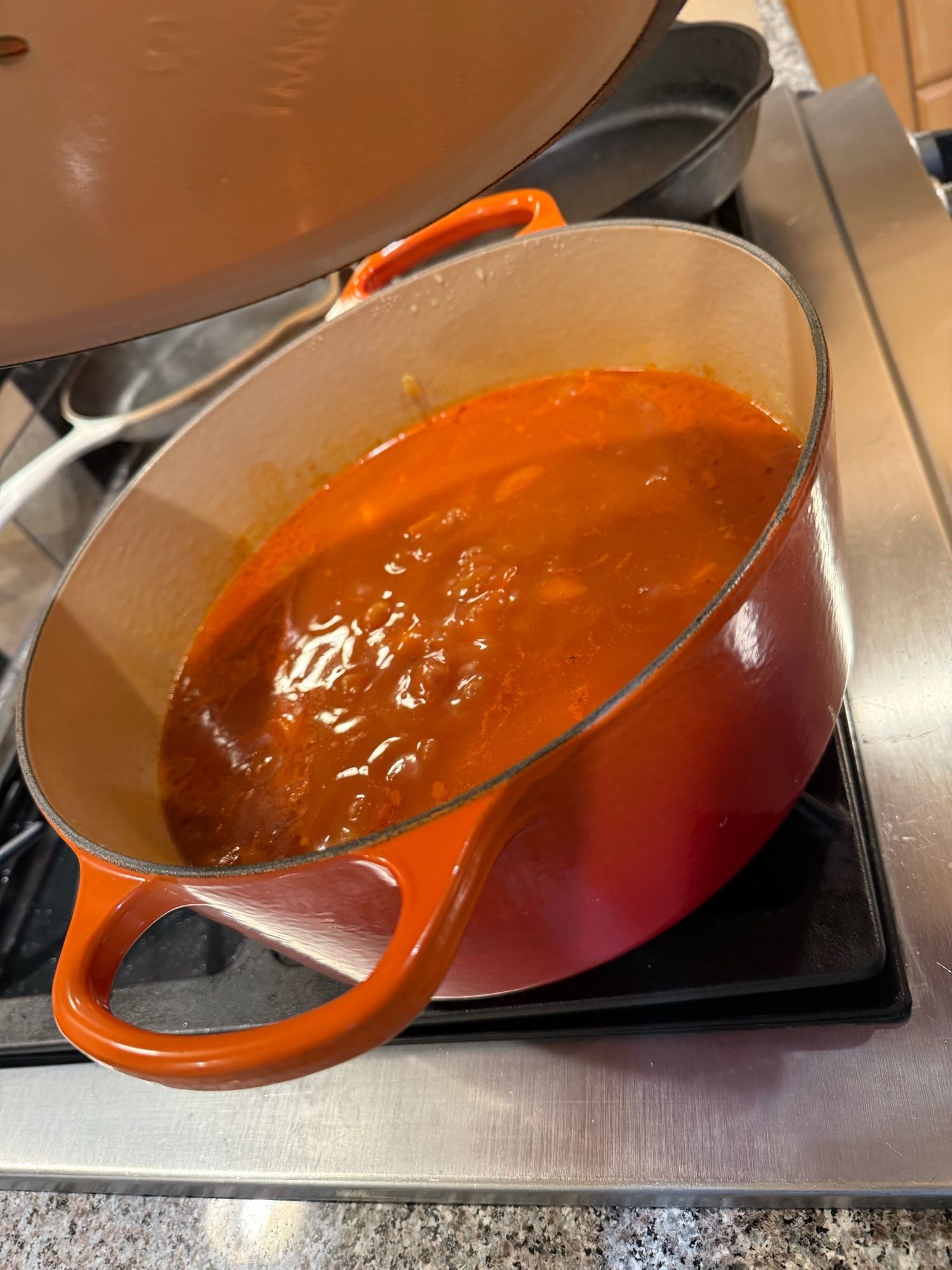 A light orange colored soup bubbling in a big orange cast iron pot.