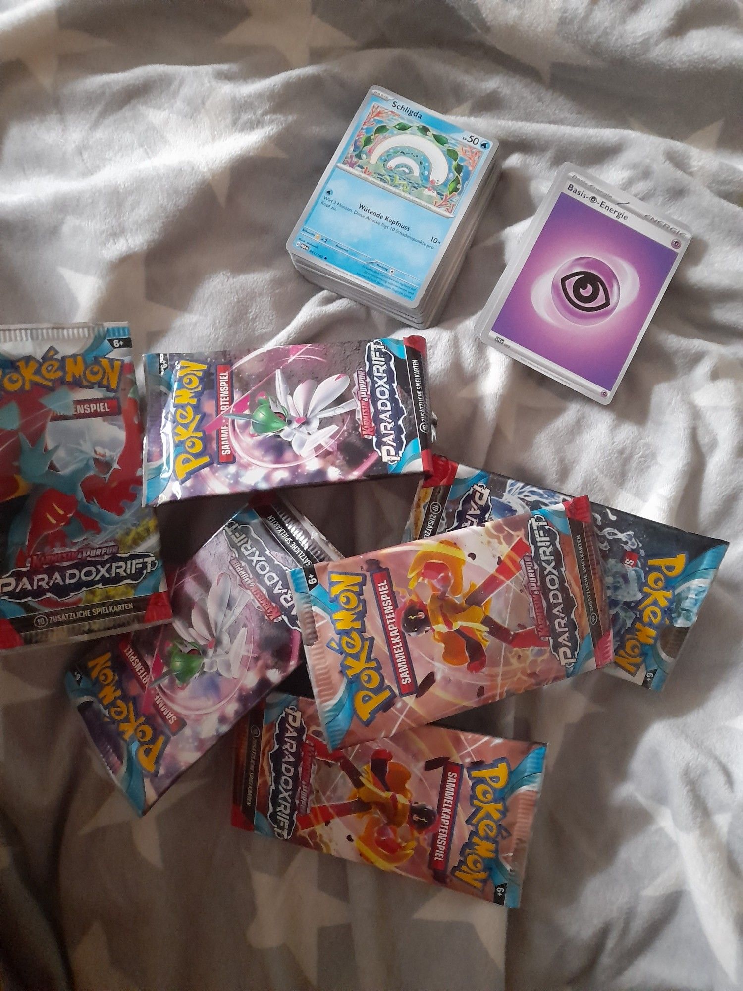 Ein Haufen geöffneter Booster-Packs des Pokémon Sammelkartenspiels (Paradoxrift), ein Stapel Energiekarten und ein Stapel mit den gezogenen Sammelkarten.