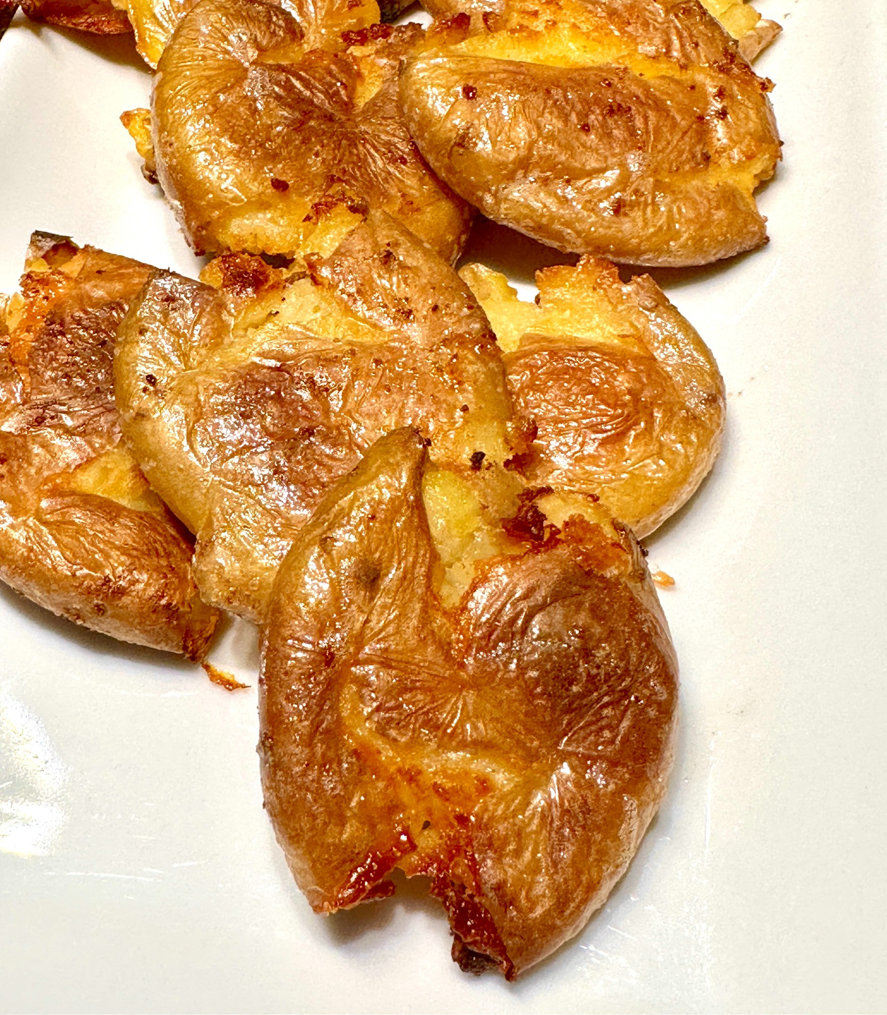 a photo of smosh potato showing several yukon gold potato that have been roasted, smoshed, and roasted again on a white plate